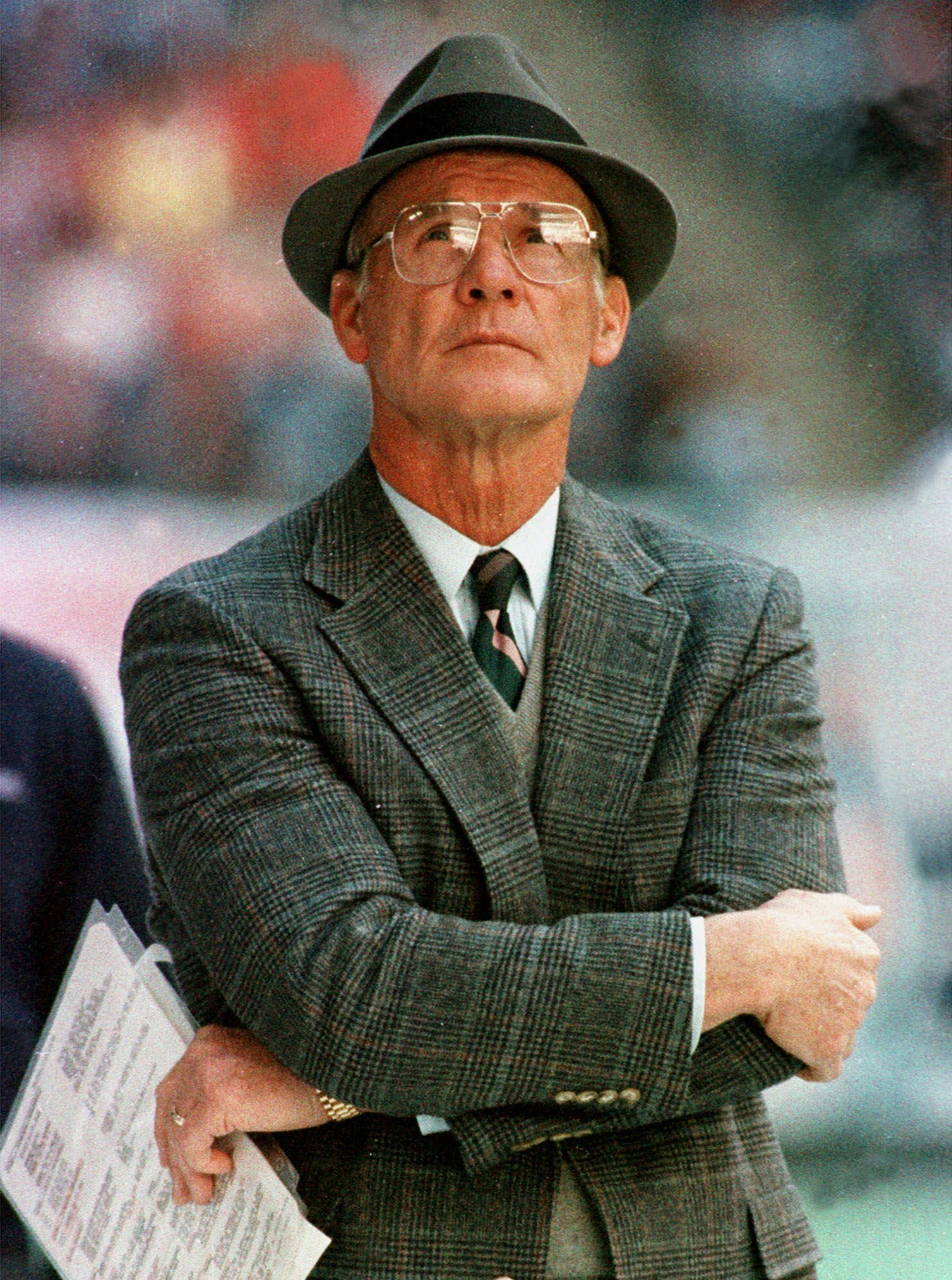 Der legendäre NFL-Coach Tom Landry, der am Spielfeldrand steht und ein karriertes Sakko mit Hut, Krawatte und Brille trägt