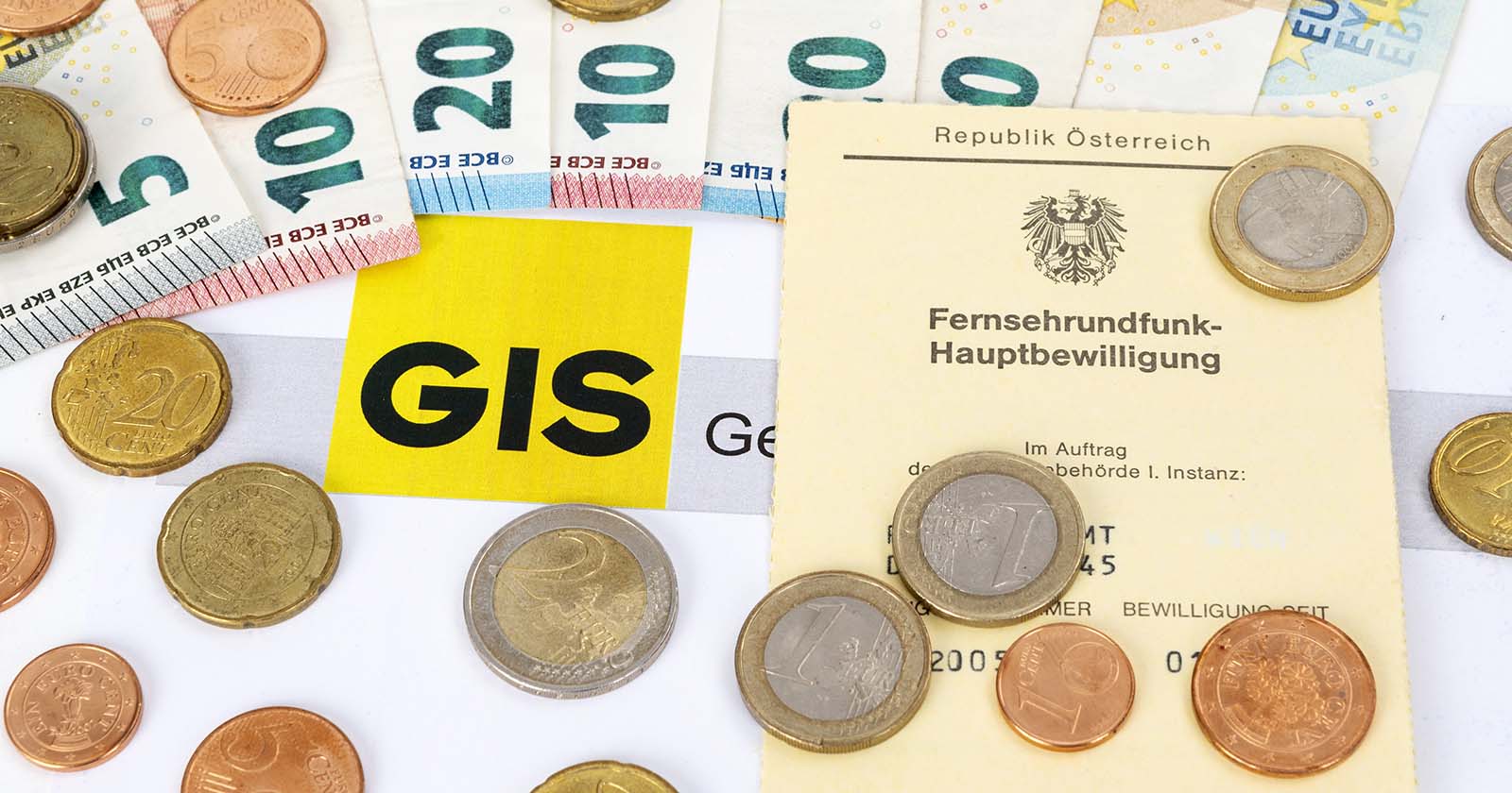 Euromünzen und Geldscheine liegen auf einem GIS-Logo