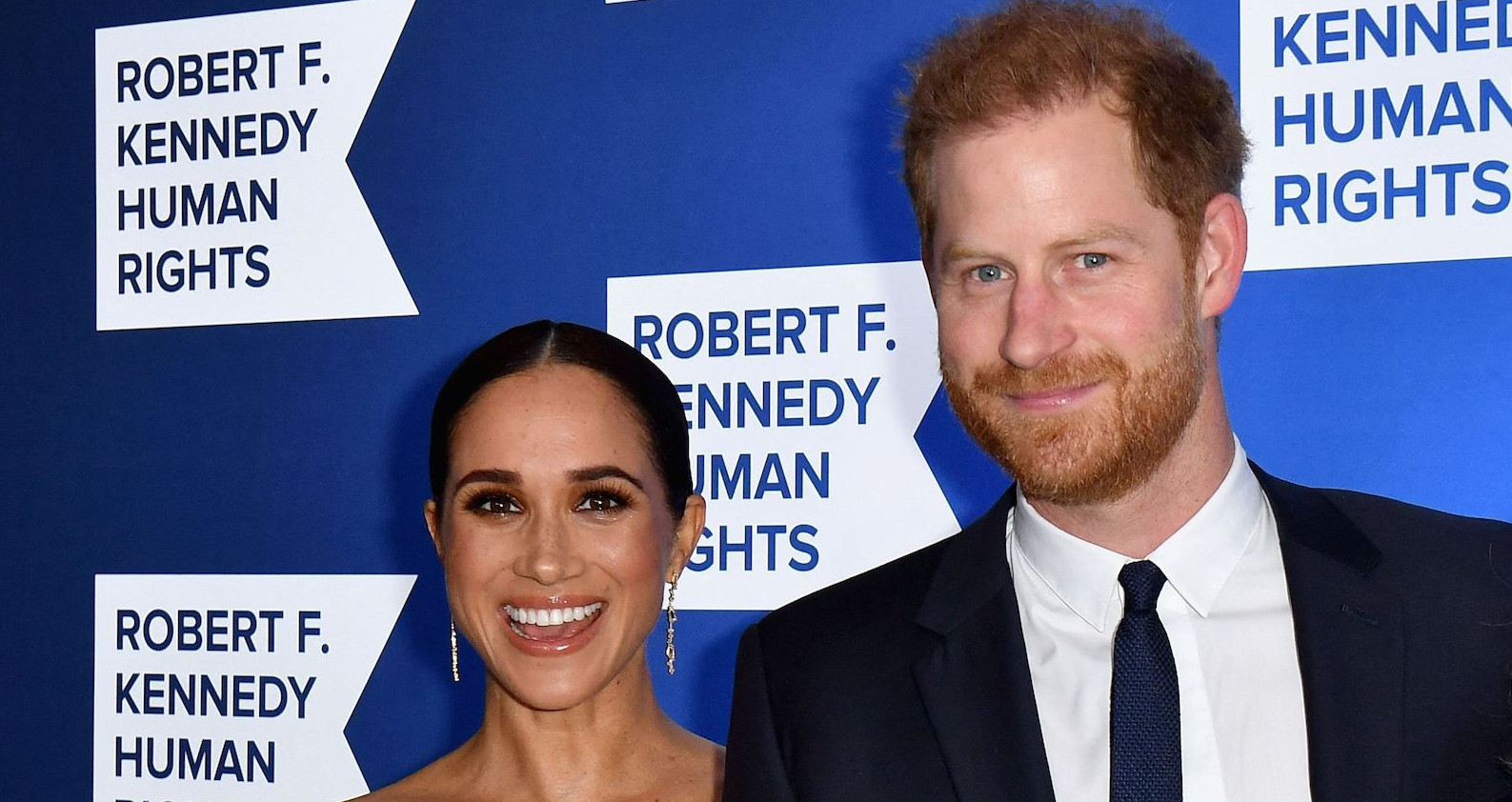 Harry und Meghan lachen mit Abendkleidung in die Kamera