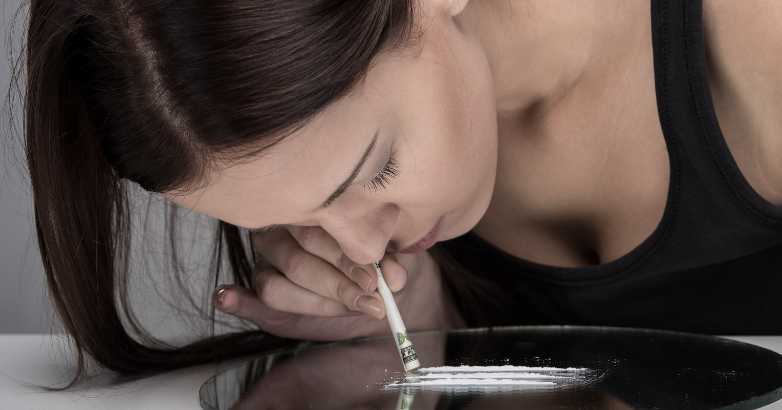 Junge Frau schnupft weißes Pulver von einem Spiegel | Credit: iStock.com/vadimguzhva