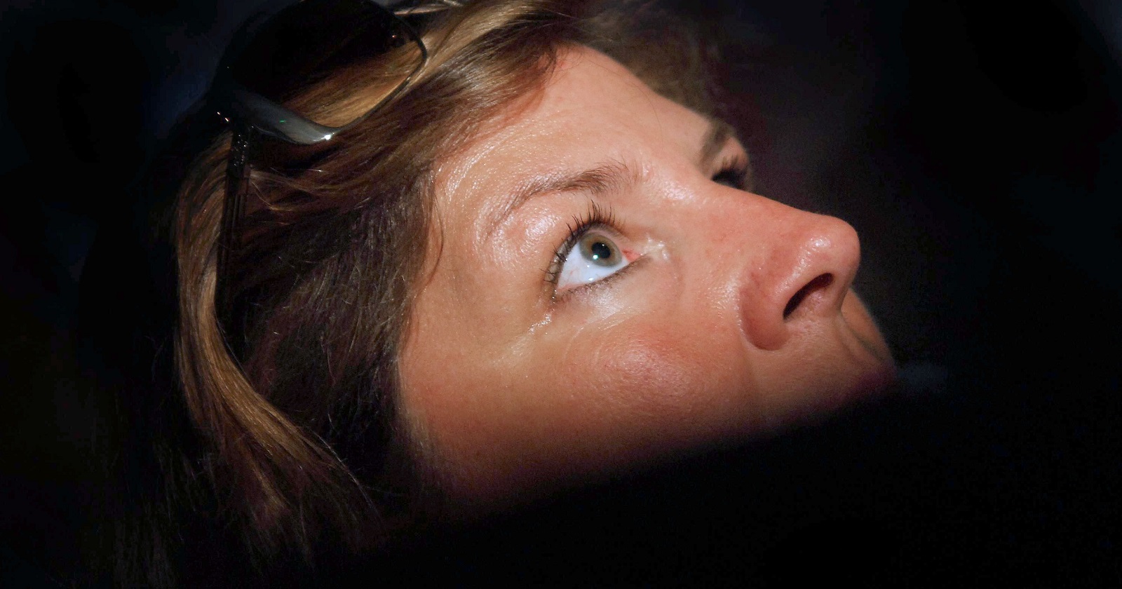 Andrea Kdolsky im Profil. Ein Schatten fällt so, dass man nur einen Teil ihres Gesichts sieht. Im Haar trägt sie eine Sonnenbrille.