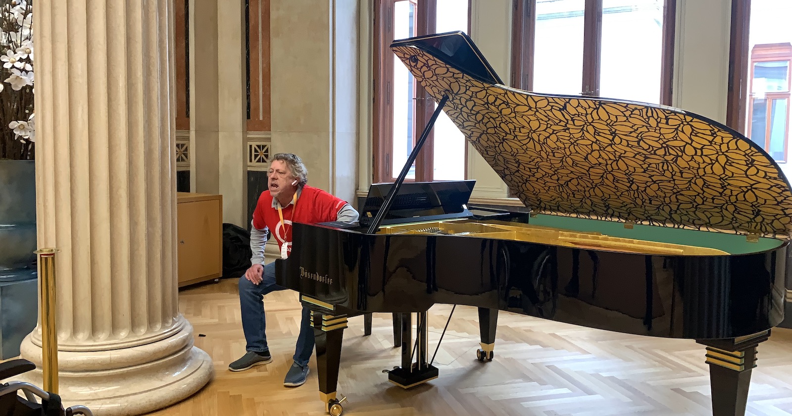 Ein älterer Mann in roten T-Shirt am Hocker des Flügels im Parlament