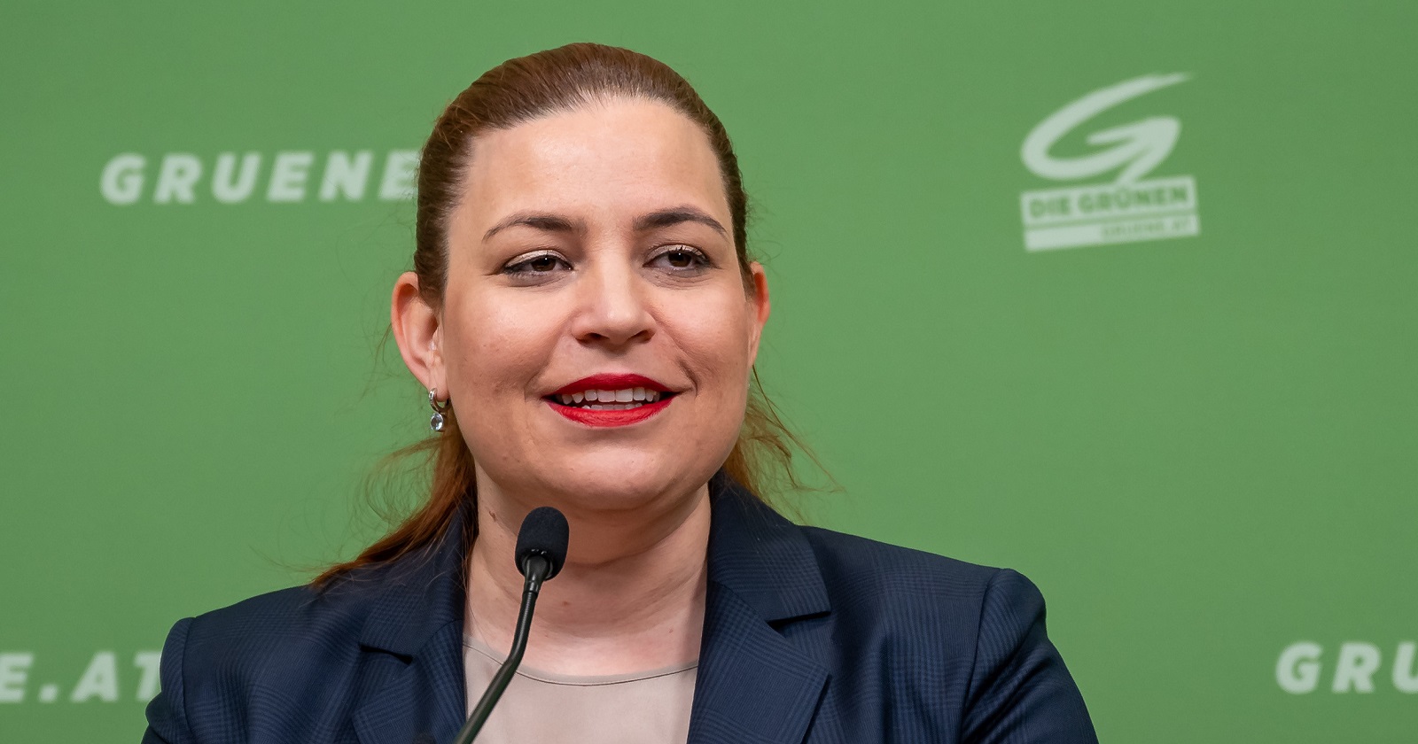 Nina Tomaselli am Rednerpult vor dem knallgrünen Pressewand-Hintergrund ihrer Partei