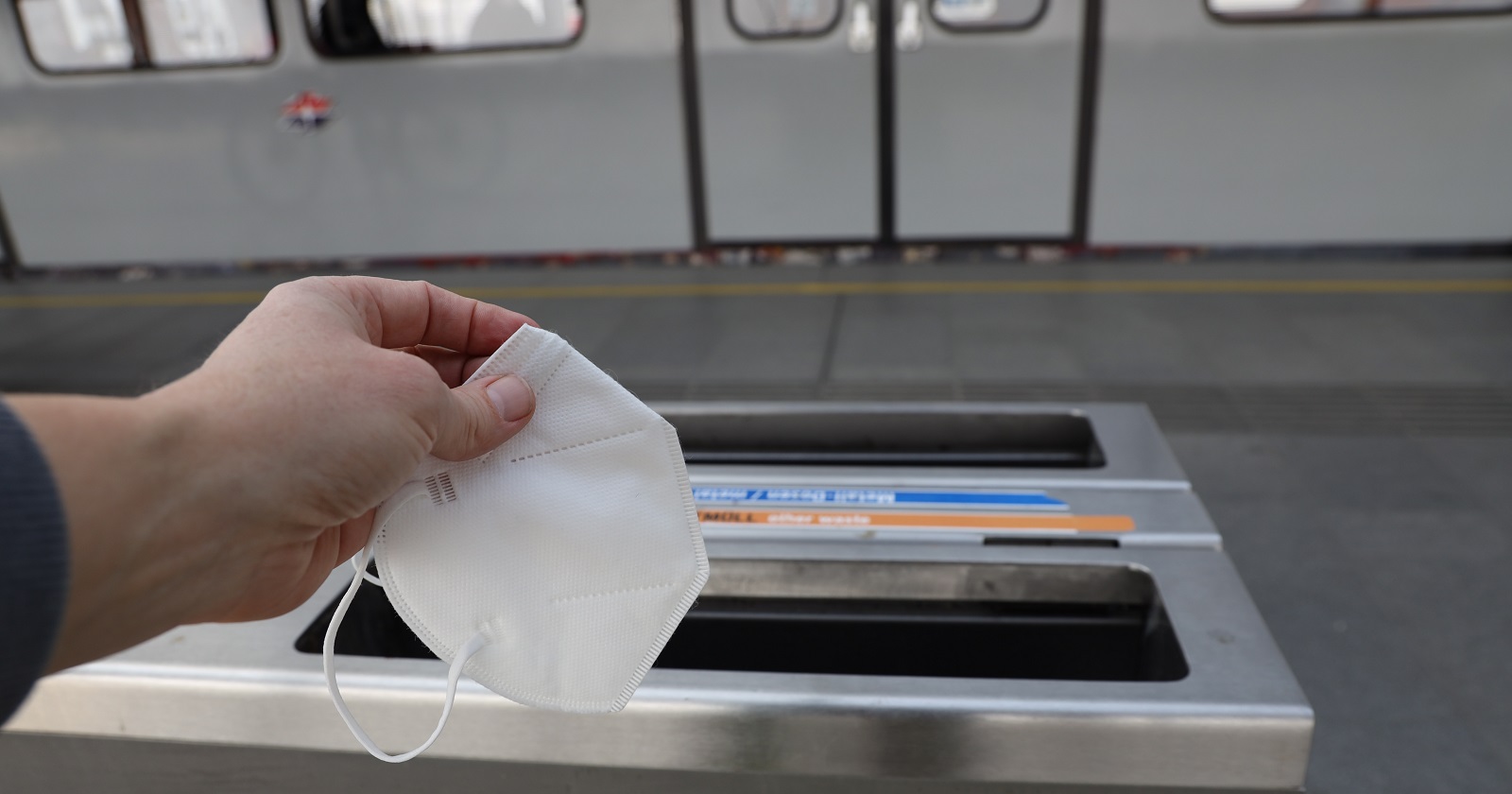 Ein Mann wirft auf einem Ubahn-Steig eine FFP2-Maske in den Mülleimer