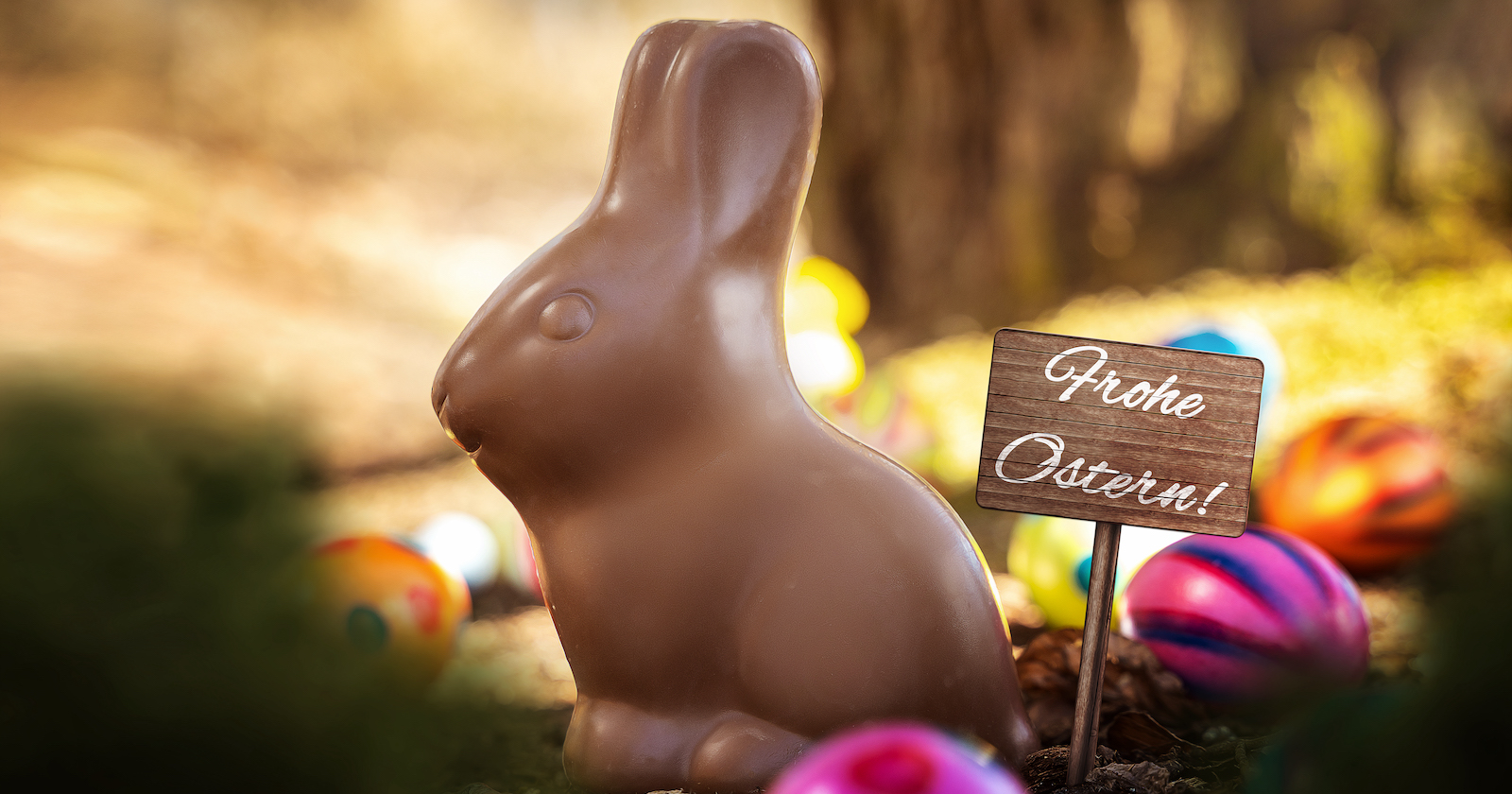 Ein Schoko-Osterhase und ein Schild, auf dem &quot;Frohe Ostern&quot; steht.