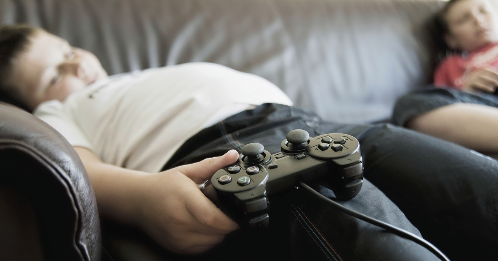 Dickes Kind liegt mit einem Controller auf dem Sofa