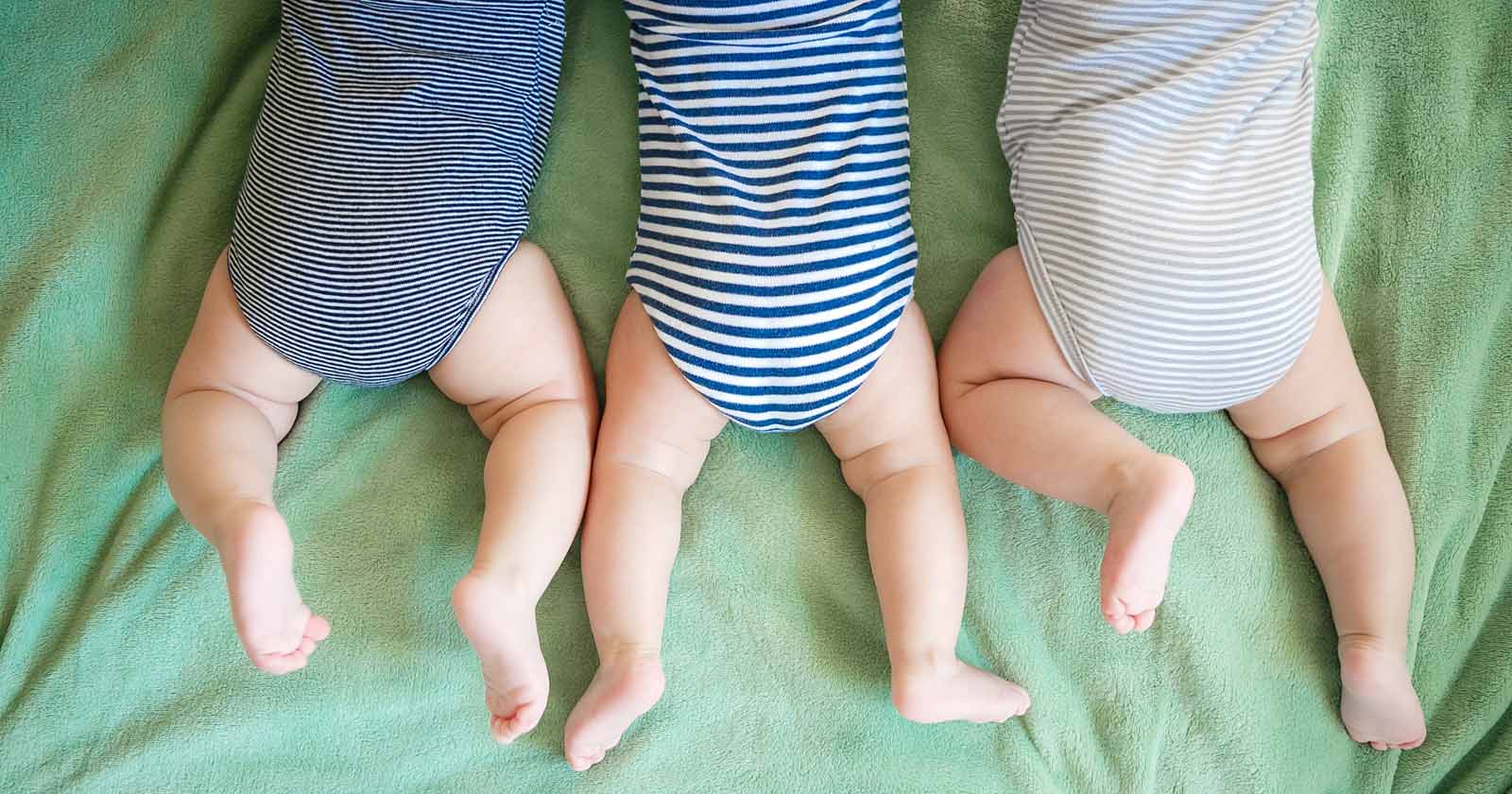 Drei Babys liegen bäuchlinks auf einer Decke