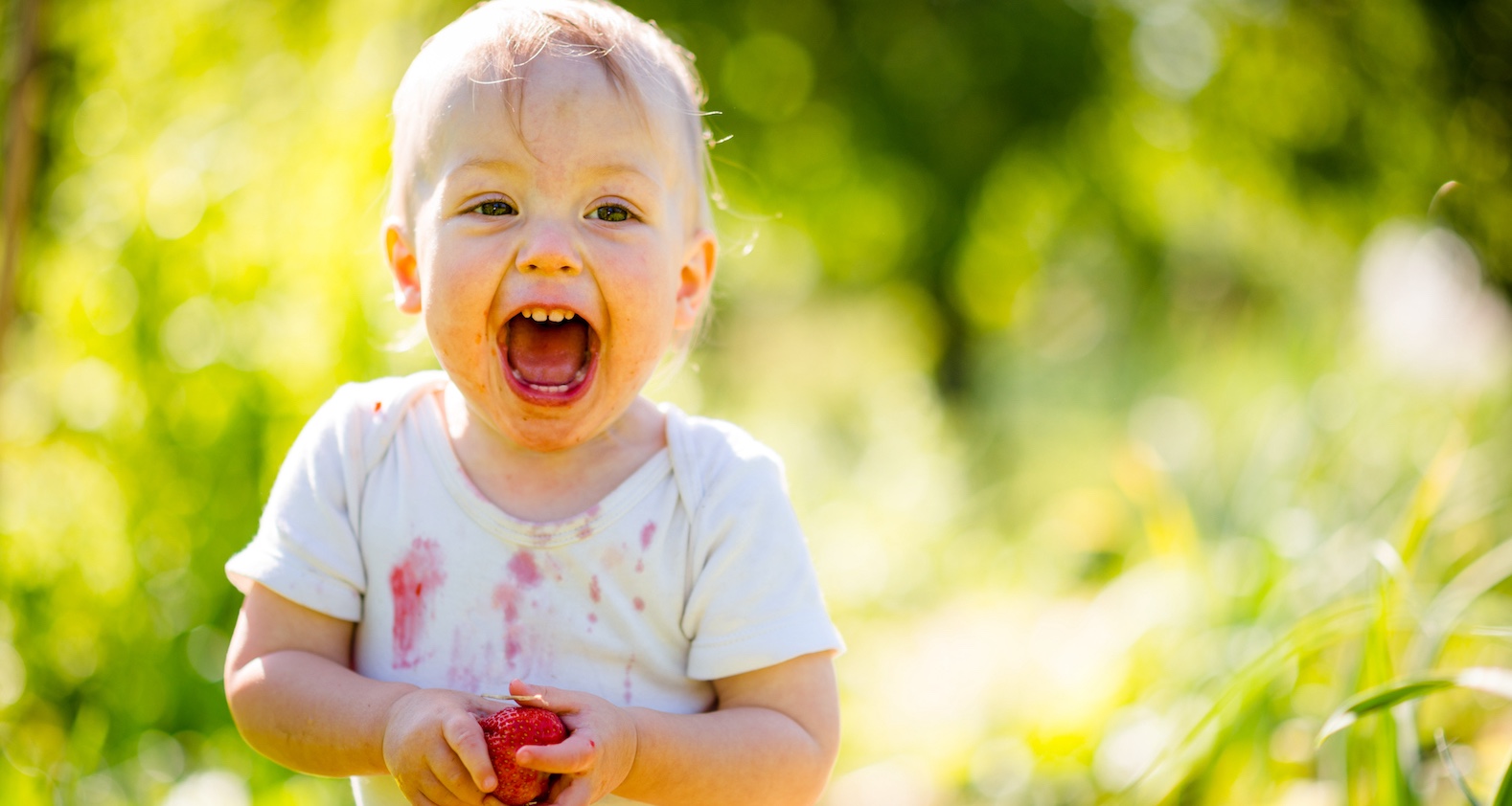 Kind isst Erdbeere und hat T-shirt voller Flecken.