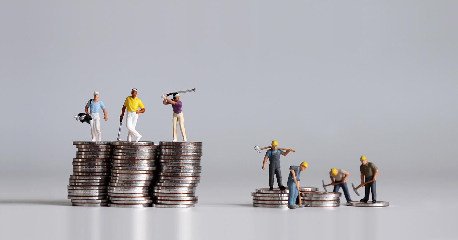 Zwei Münzhaufen. Auf dem Größeren spielen Plastikfiguren Golf. Auf dem Kleineren sind die Plastikfiguren Bauarbeiter.
