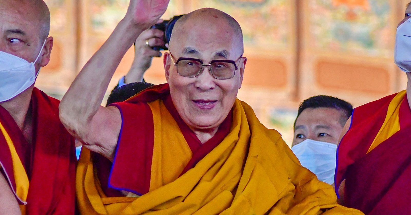 Der Dalalai-Lama umgeben von Gefolgsleuten lacht und winkt