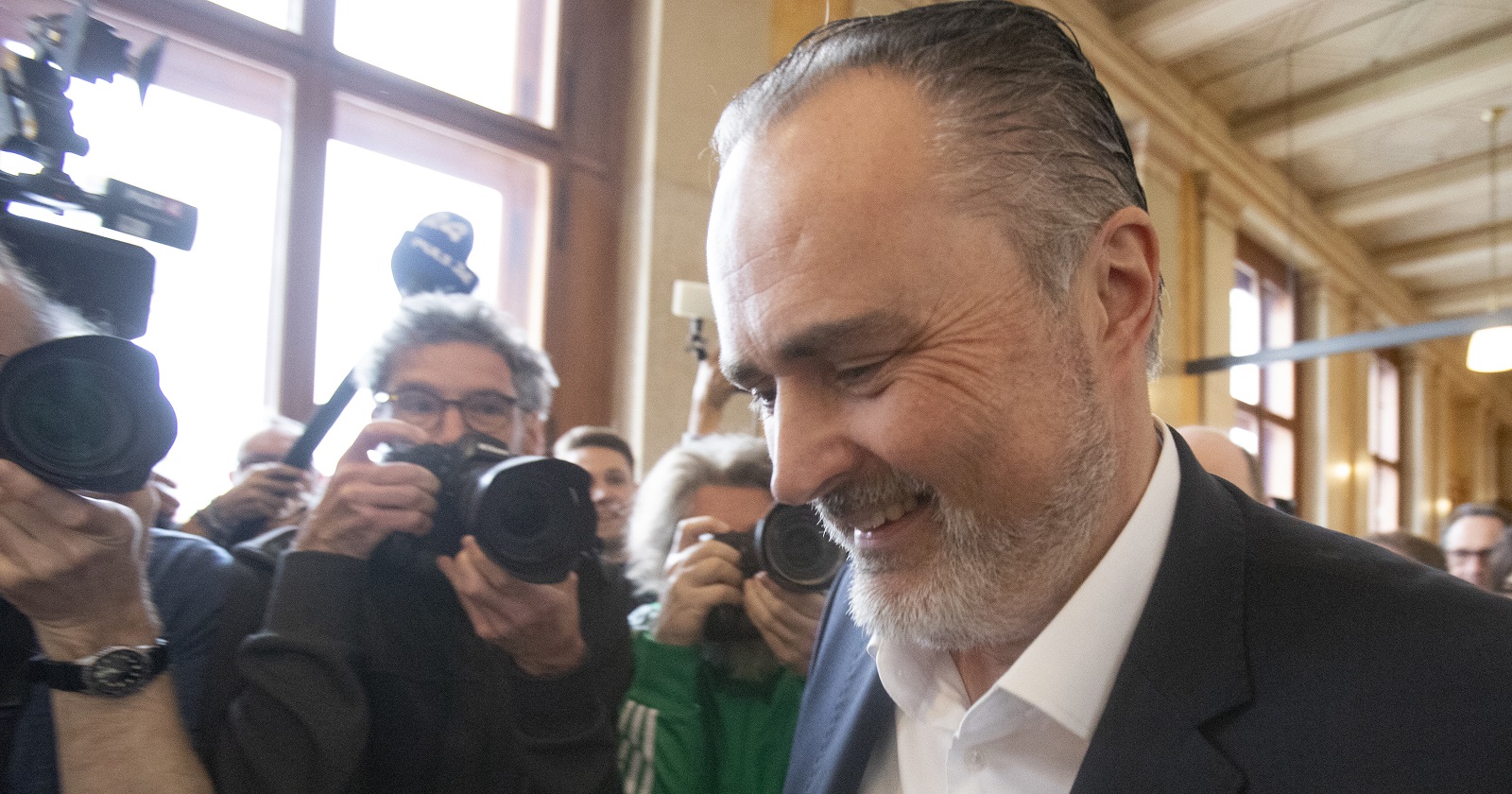 Hans Peter Doskozil im Halbporträt vor Journalisten. Er schaut leicht nach unten und lacht.