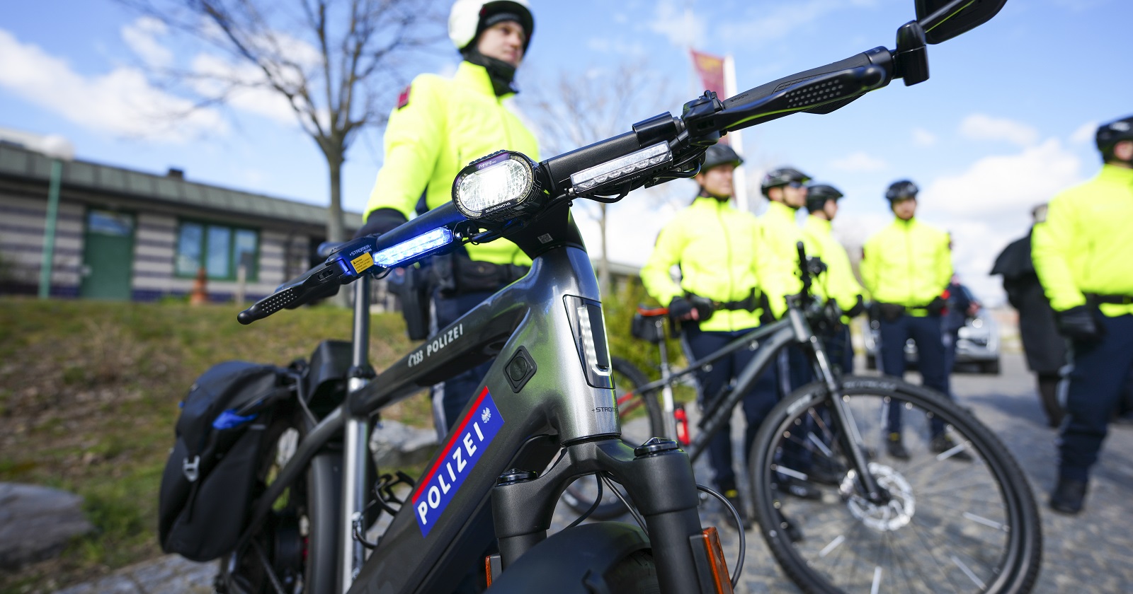Großaufnahme des Lenkers eine Polizeirades mit Blaulicht. Im Hintergrund die Beamten mit gelben Jacken und Helm