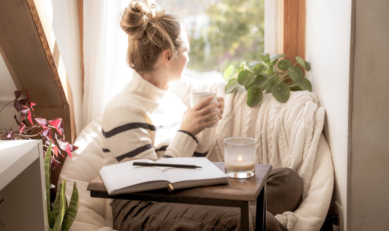 Frau sitzt in ihrer Kuschelecke und schaut aus dem Fenster | Credit: iStock.com/Elle Mundus