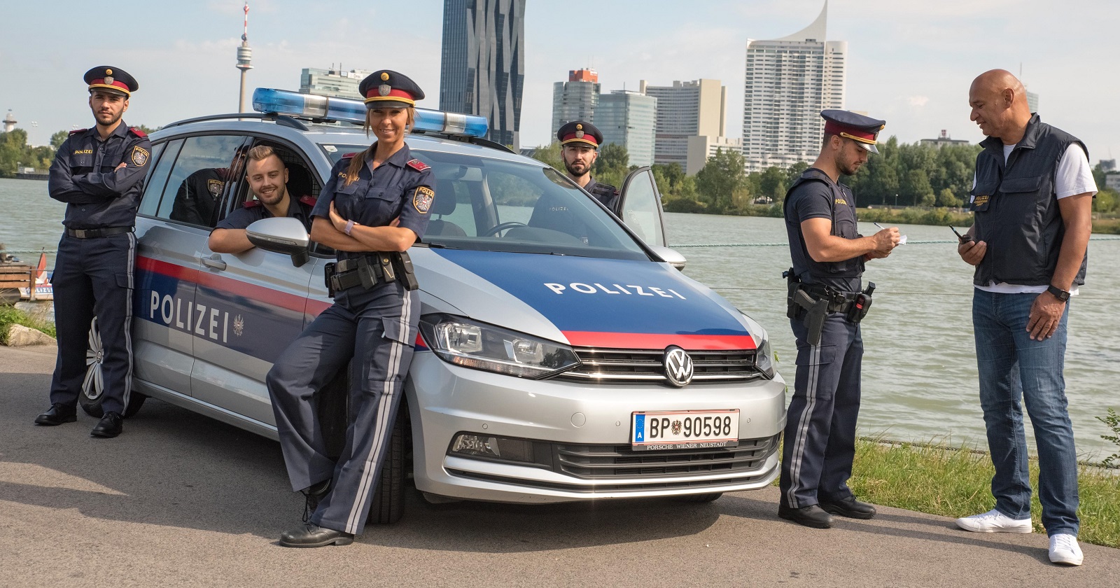 Polizisten stehen vor und um ein Polizeiauto an der Donau in Wien. Am anderen Ufer ist der DC-Tower zu sehen.
