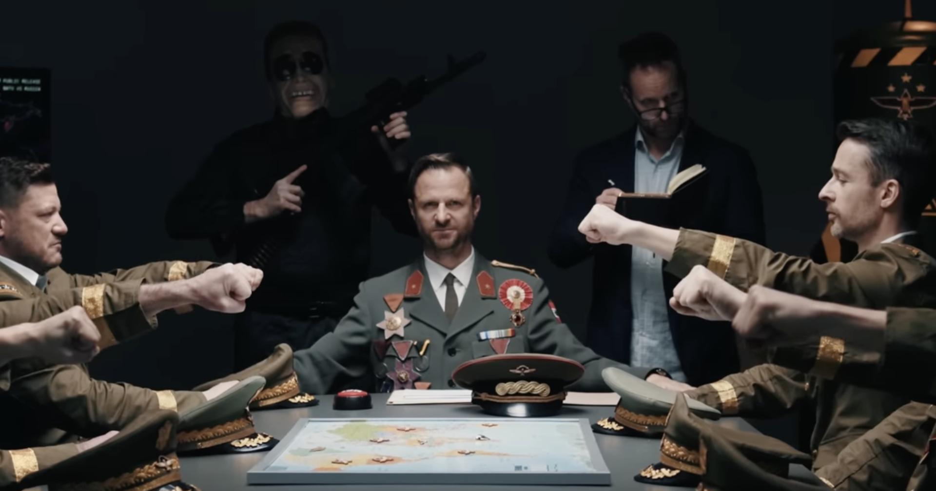 Hochmair in Uniform an einem Tisch mit Generälen. Hinter ihm schreibt Strolz in ein Buch