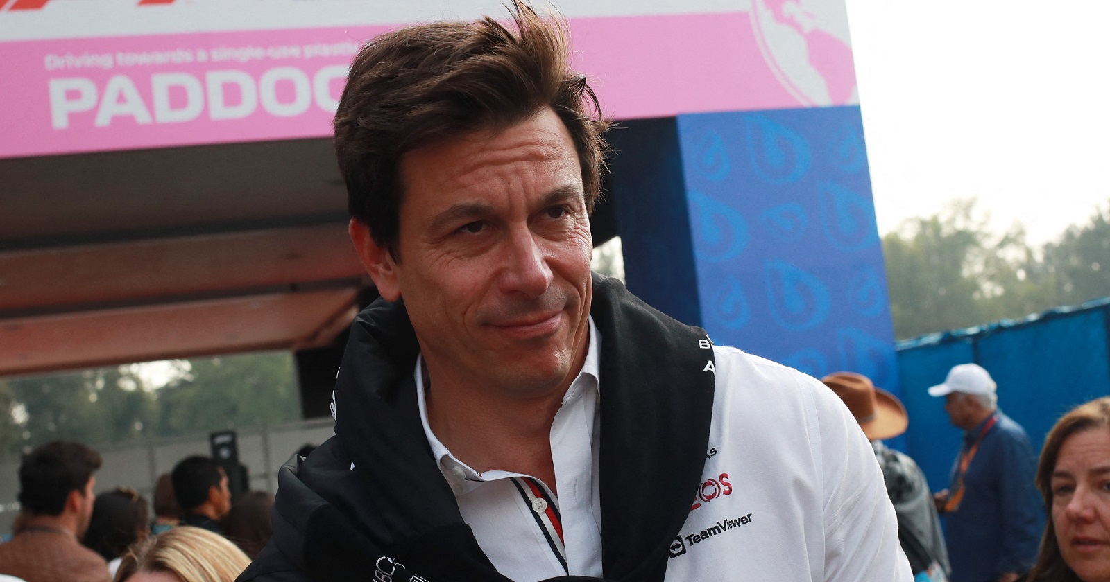 Toto Wolff in Großaufnahme am Rande der Rennstrecke. Er trägt ein weißes Hemd, über den Schultern hängt vor der Brust verknotet ein schwarzer Sweater.