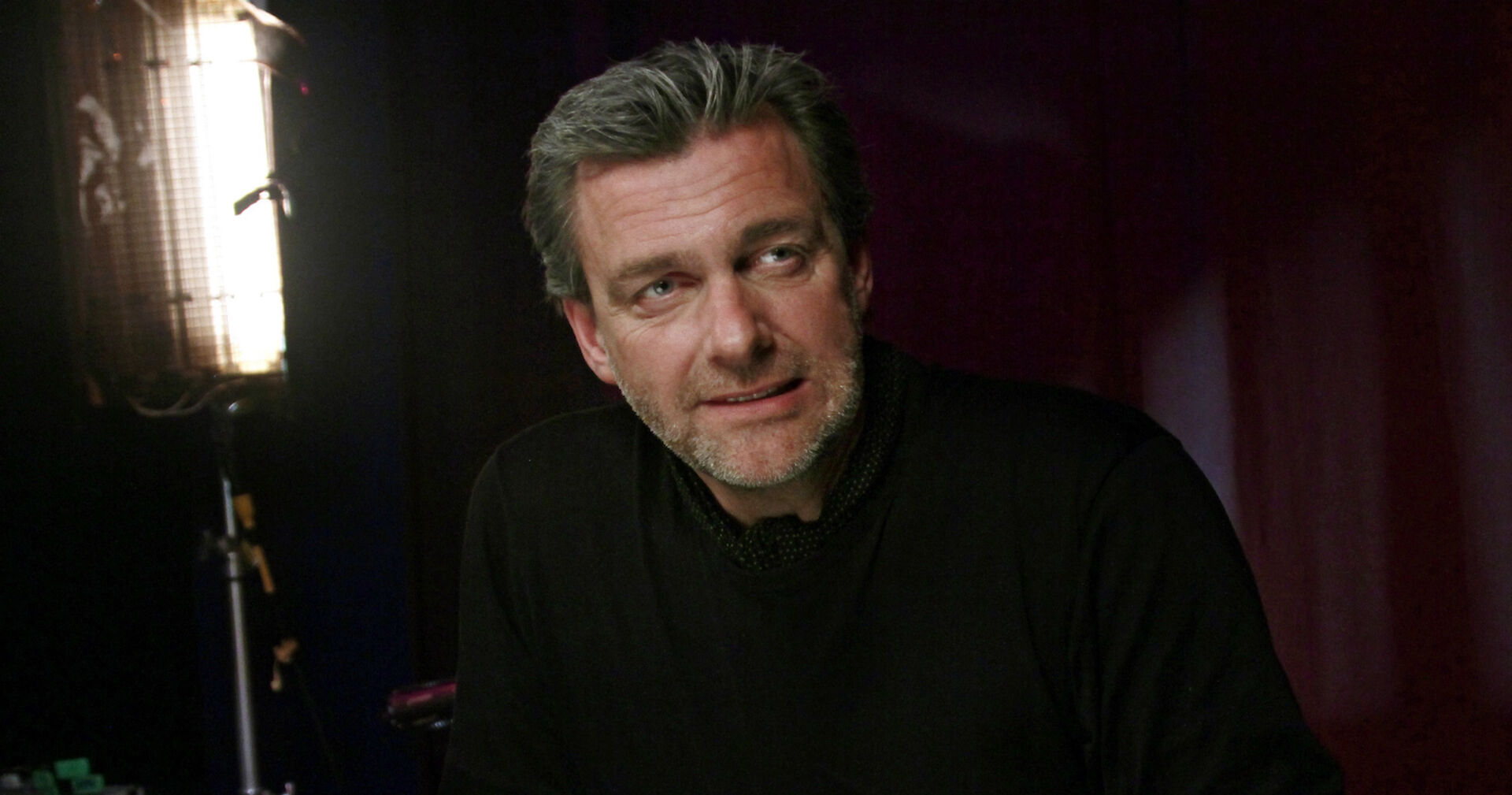 Ray Stevenson in schwarzem Pullover bei einem Interview.