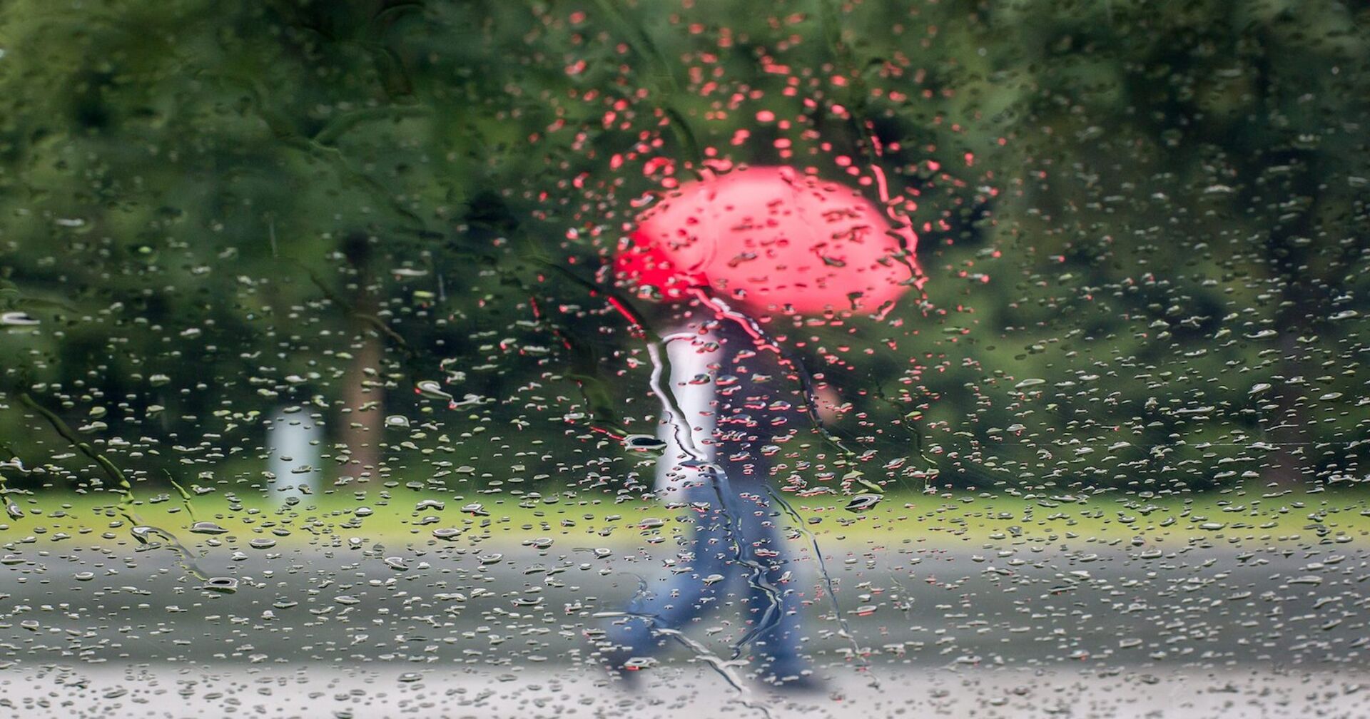 Jemand geht im Regen mit einem roten Schirm spazieren.
