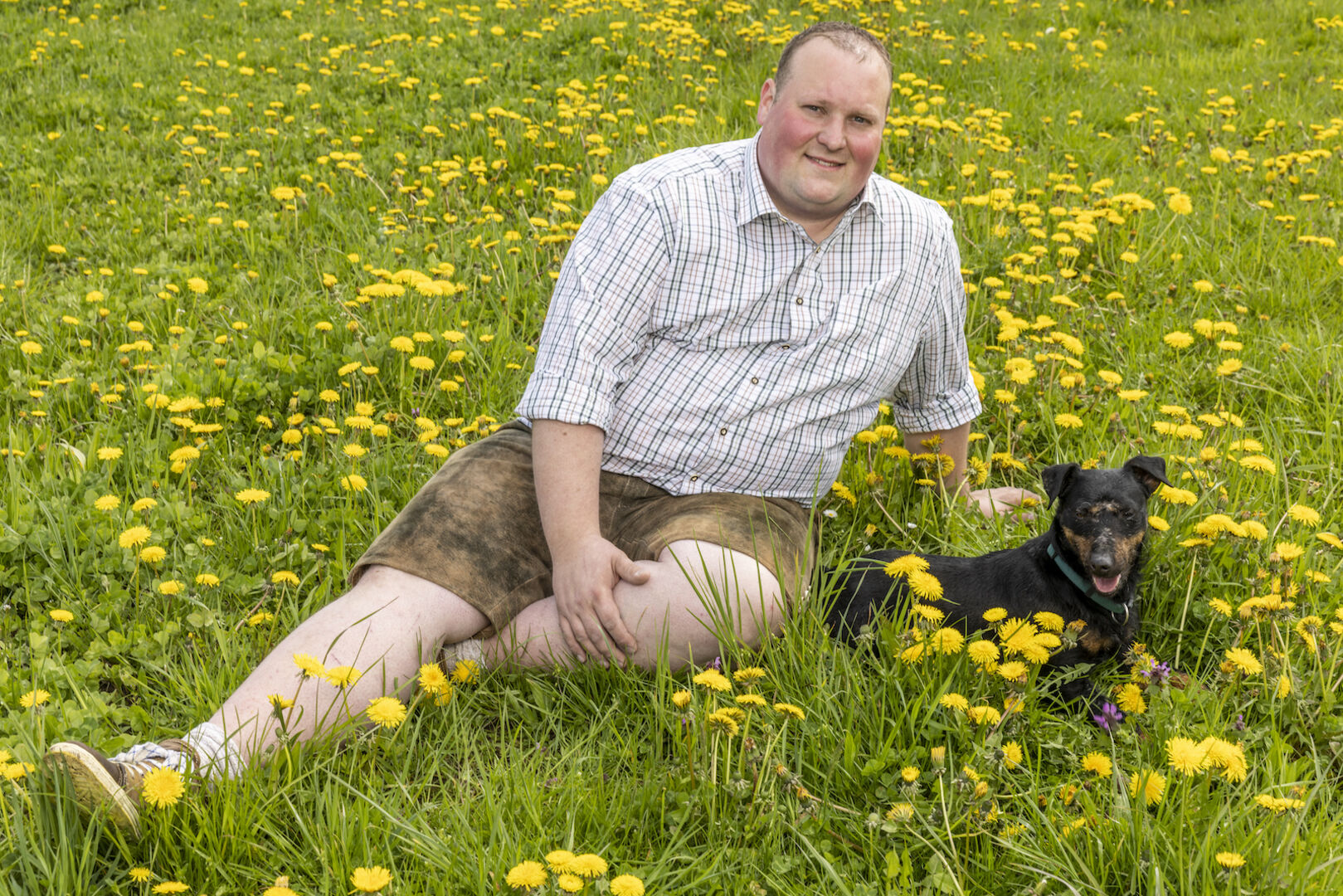Christoph sitzt mit seinem Hund in der Blumenwiese