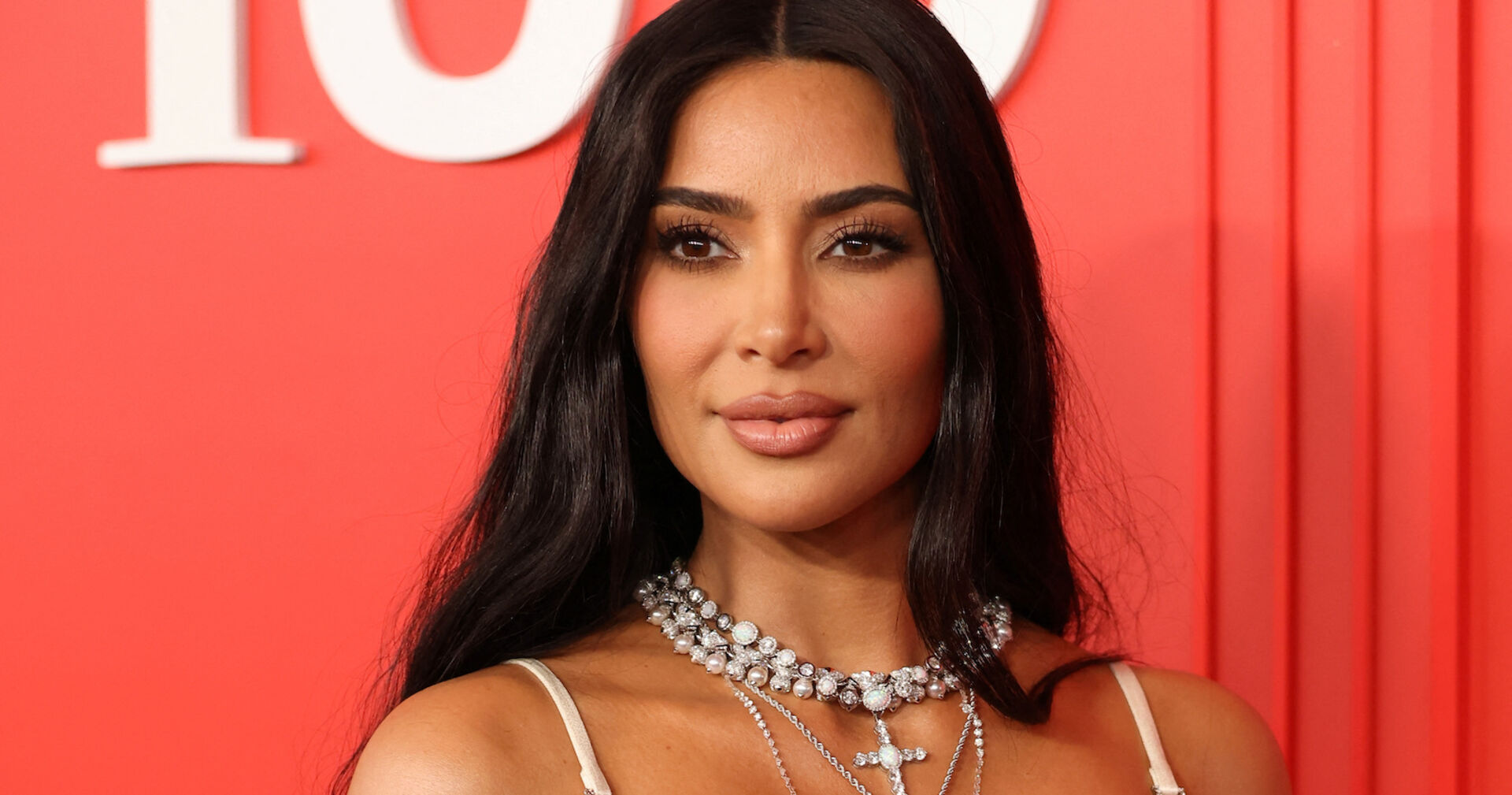 Kim Kardashian vor rotem Hintergrund mit tiefem Dekolleté und vielen Ketten