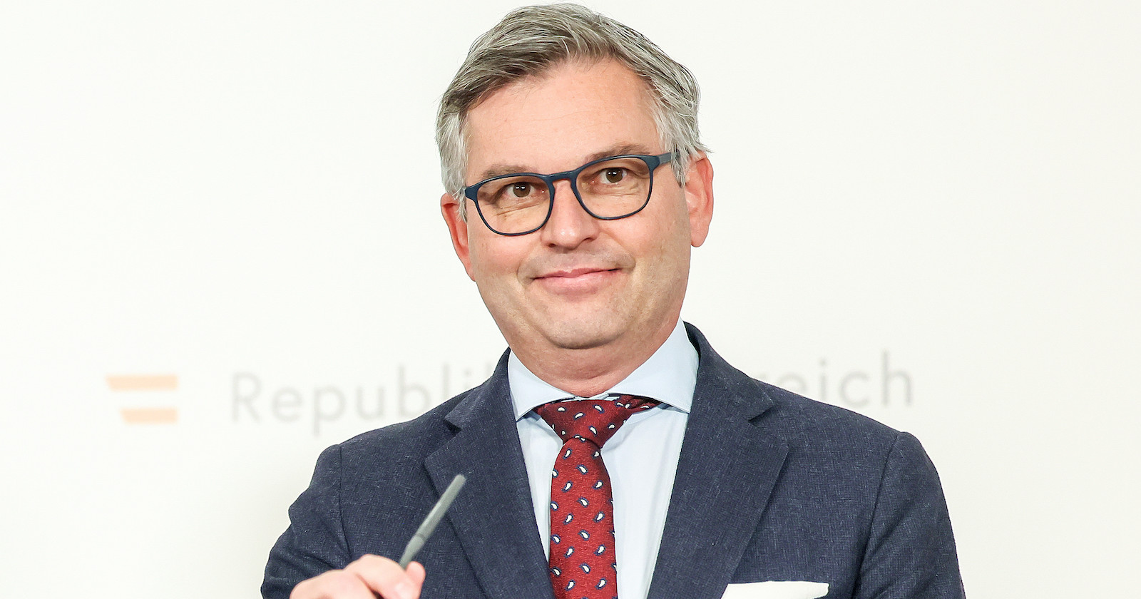 Magnus Brunner vor der Pressewand des FInanzminiteriums. Er grinst schelmisch