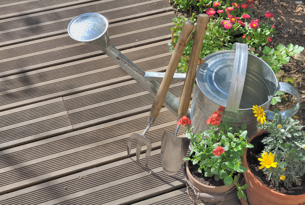 Gießkanne steht auf einem Balkon.