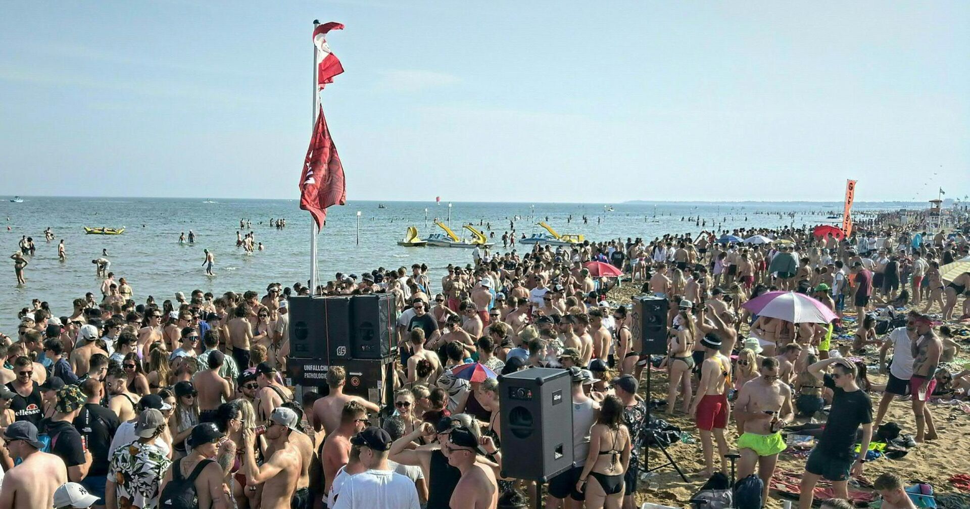 Eine Party am Strand von Lignano. Boxen, viele Menschen in Badekleidung und eine österreichische Flagge