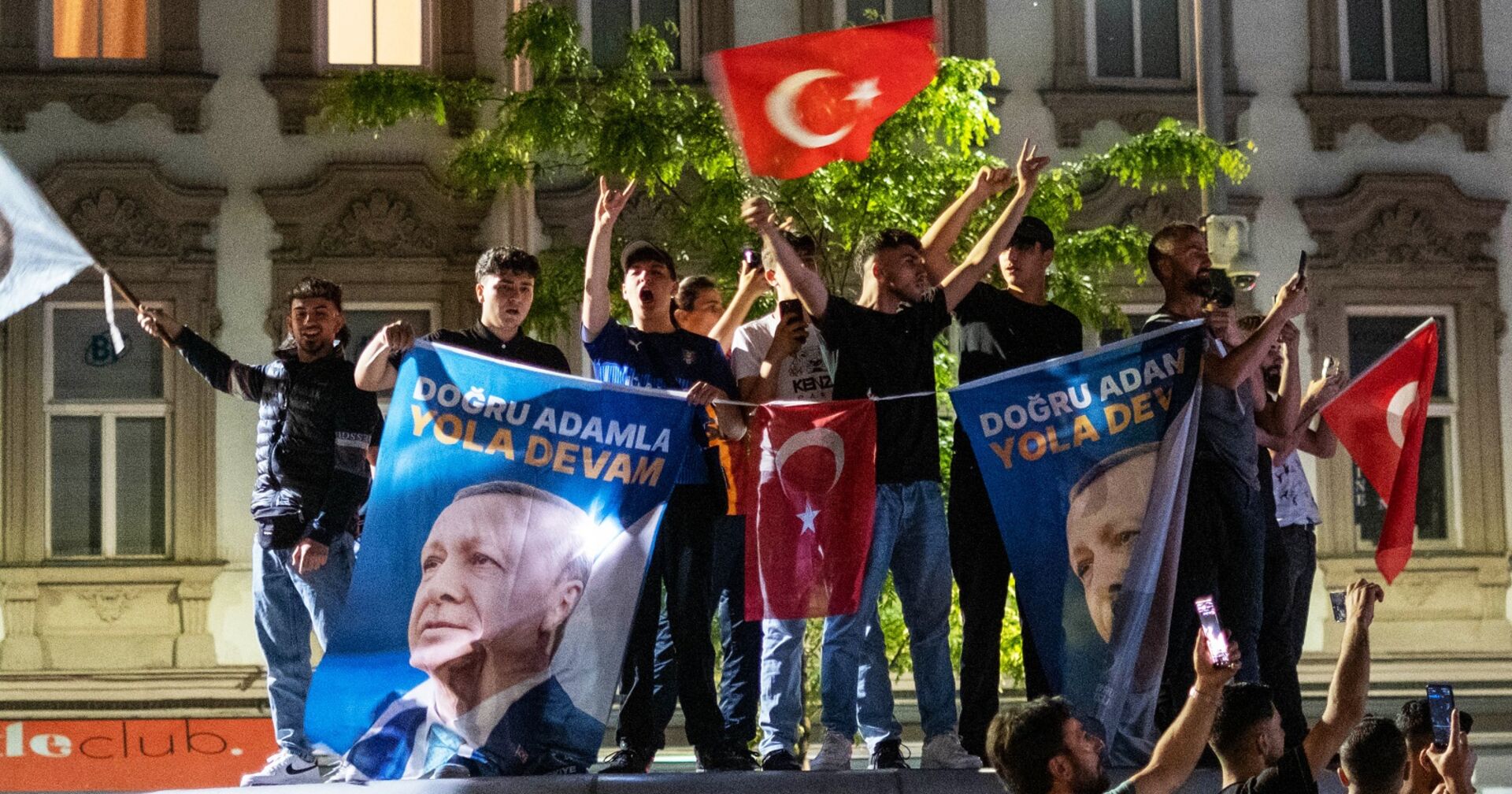 Aufnahme bei Nacht. Jugendliche und junge Männer schwenken ausgelassen türkische Fahnen und hissen Transparente mit Erdogans Porträt.
