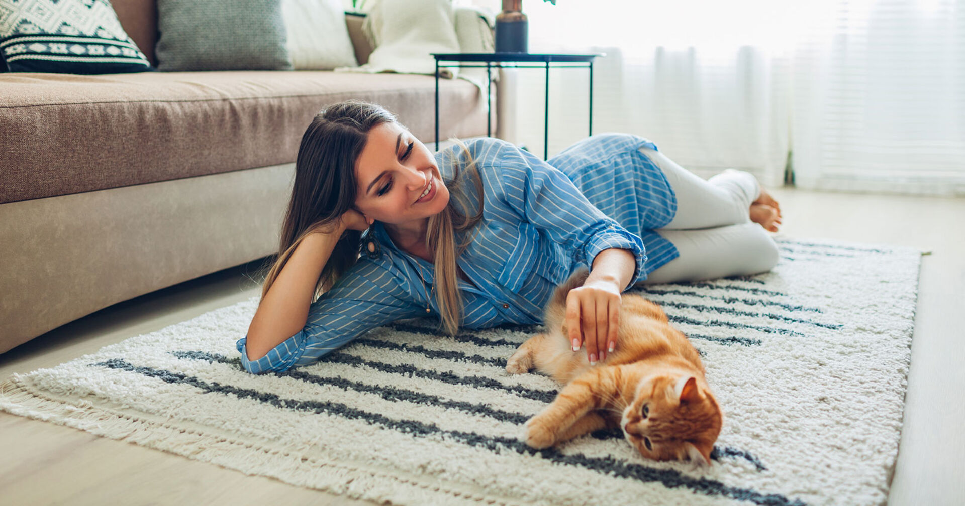 Junge Frau liegt mit ihrer Katze ausgestreckt auf dem Teppich | Credit: iStock.com/Maryviolet