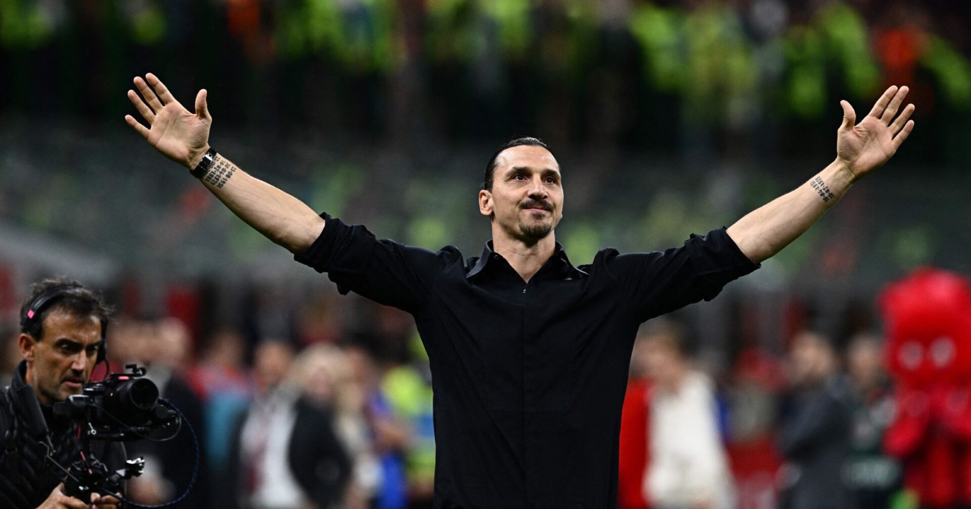Der ganz in schwarz gekleidete Zlatan Ibrahimović mit weit ausgebreiteten Armen vor der Kulisse des Heimstadions des AC Milan