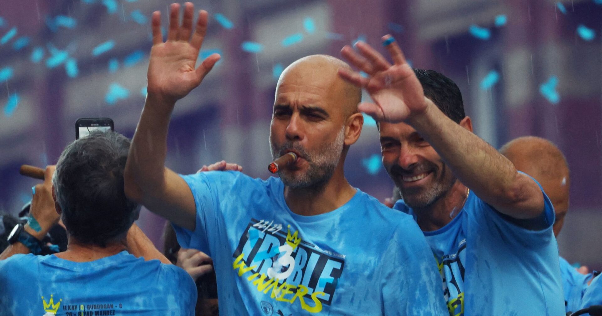 Der eine Zigarre rauchende Pep Guardiola, der auf der Siegesfeier von Manchester City in einem türkisen Konfettiregen steht und winkt