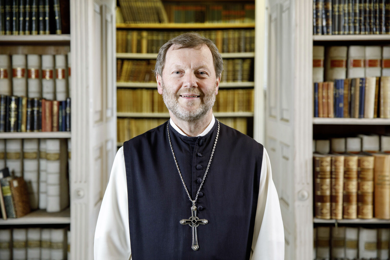 Pater Reinhold Dessl vor Bücherregalen der Stiftsbibliothek.