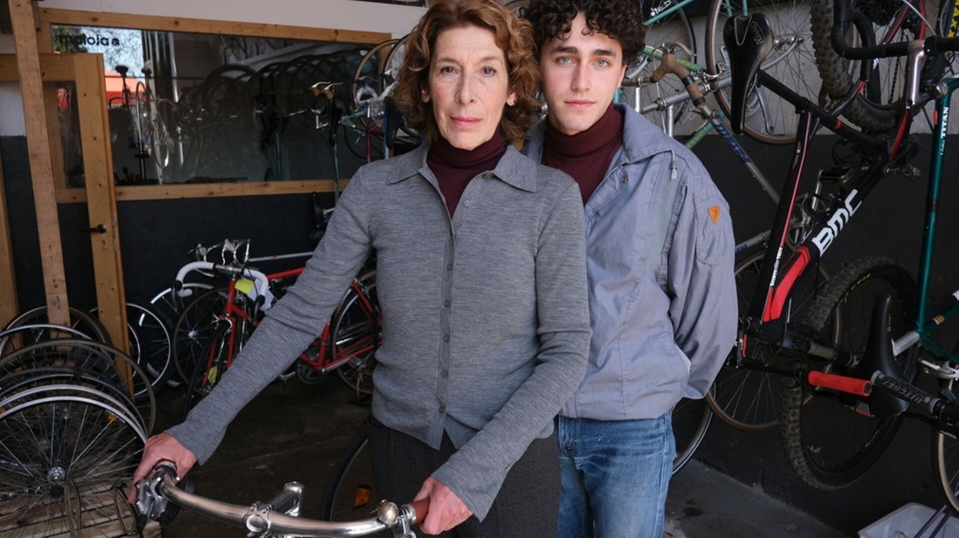 Adele Neuhauser mit einem Fahrrad und einem jungen Mann an der Seite