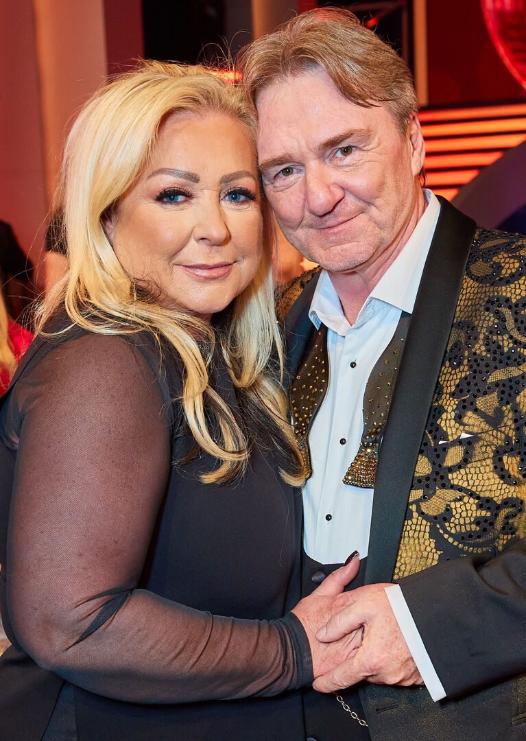 Ein Mann und eine blonde Frau lächeln in die Kamera.