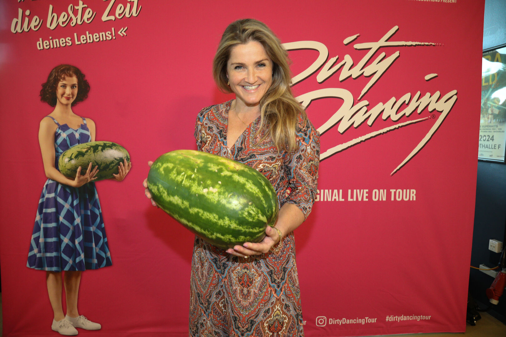 Lizz Görgl vor einem Plakat mit einer Melone in der Hand.
