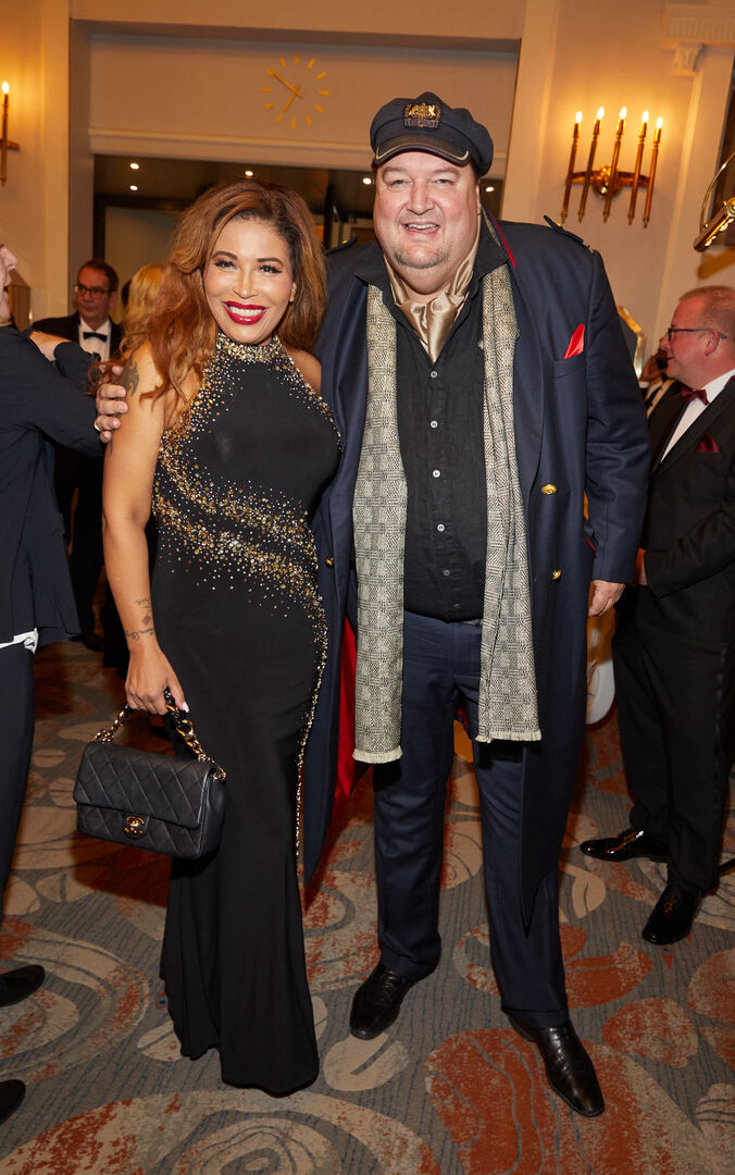 Ein sehr dicker Mann mit Kapitänsmütze steht neben einer Frau im Ballkleid.