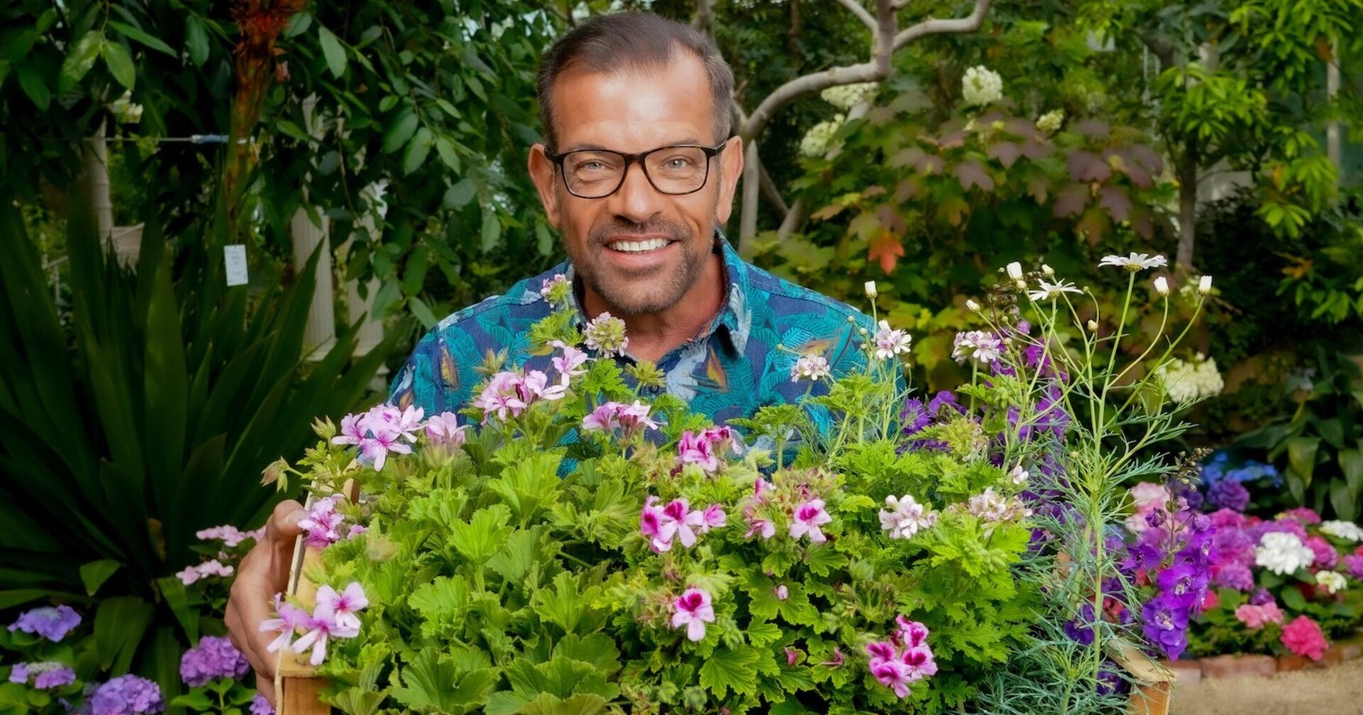Karl Ploberger hält im Garten eine Holzkiste mit blühenden Sommerblumen | Credit: ORF/Roman Zach-Kiesling