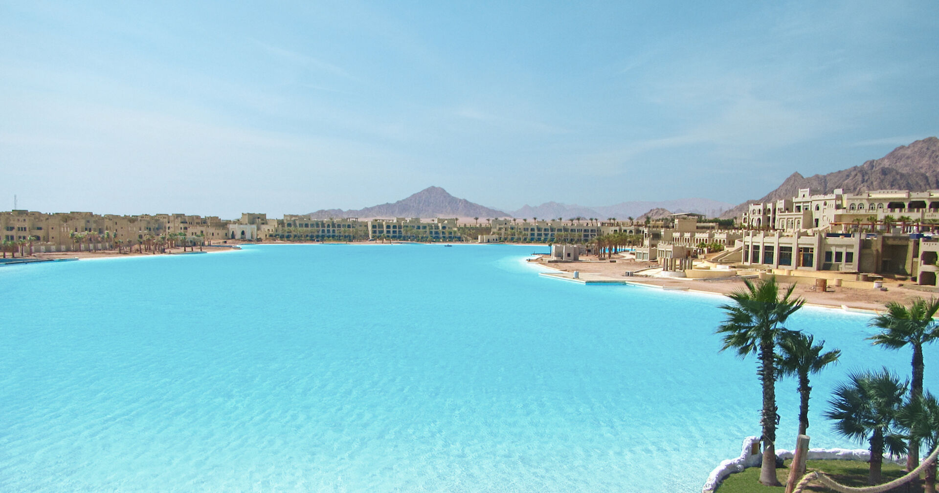 Riesiger hellblauer Pool, an deren Ufer sich im Bau befindliche Hotels reihen