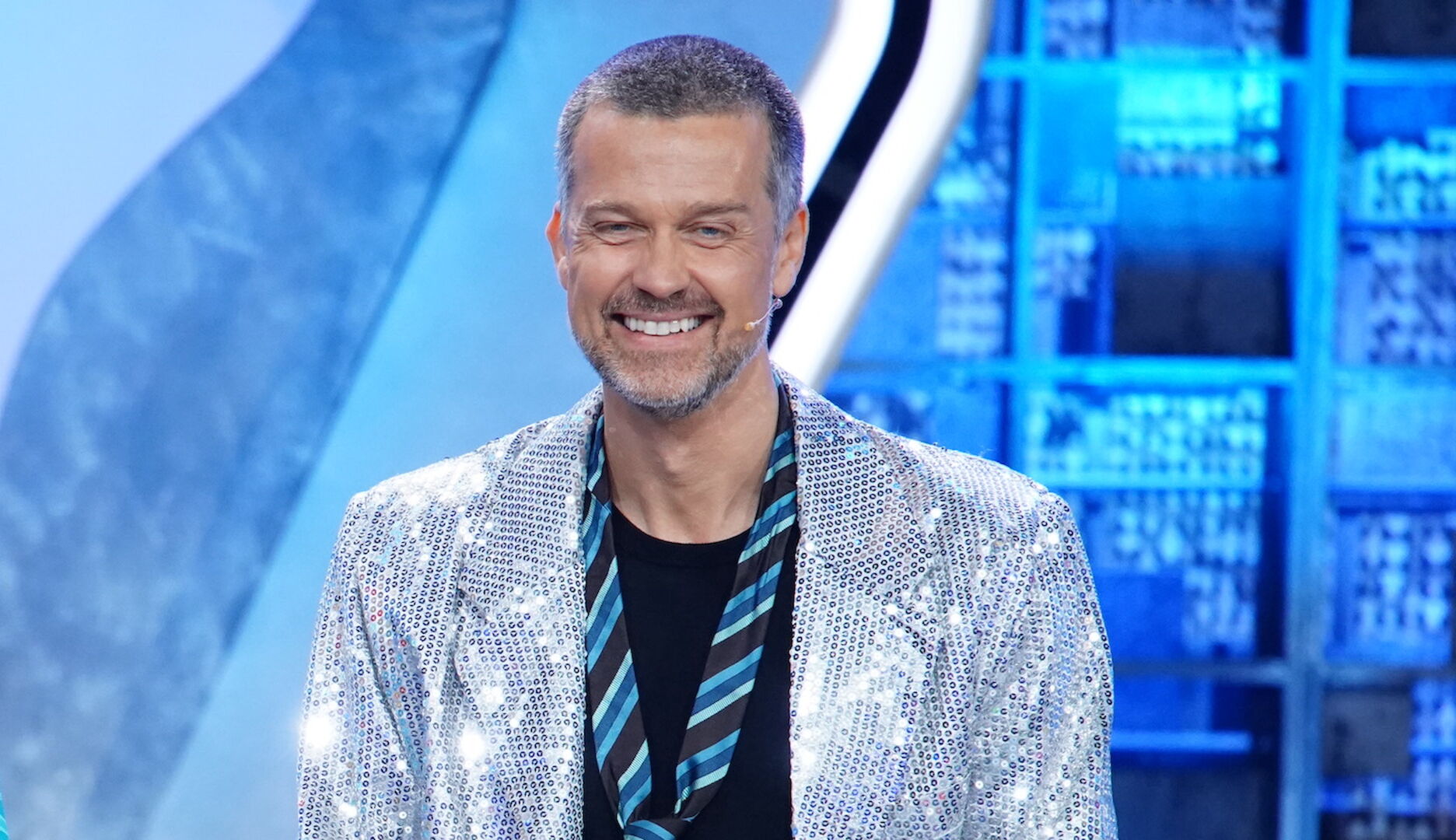Ein Mann mit einem Glitzersakko und einer Krawatte ganz lässig umgebunden