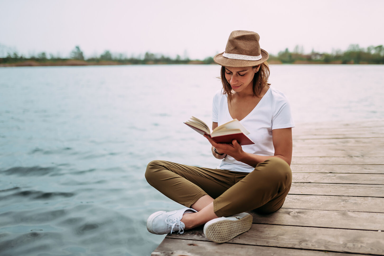 Frau sitzt am See und liest ein Buch | Credit: iStock.com/nortonrsx