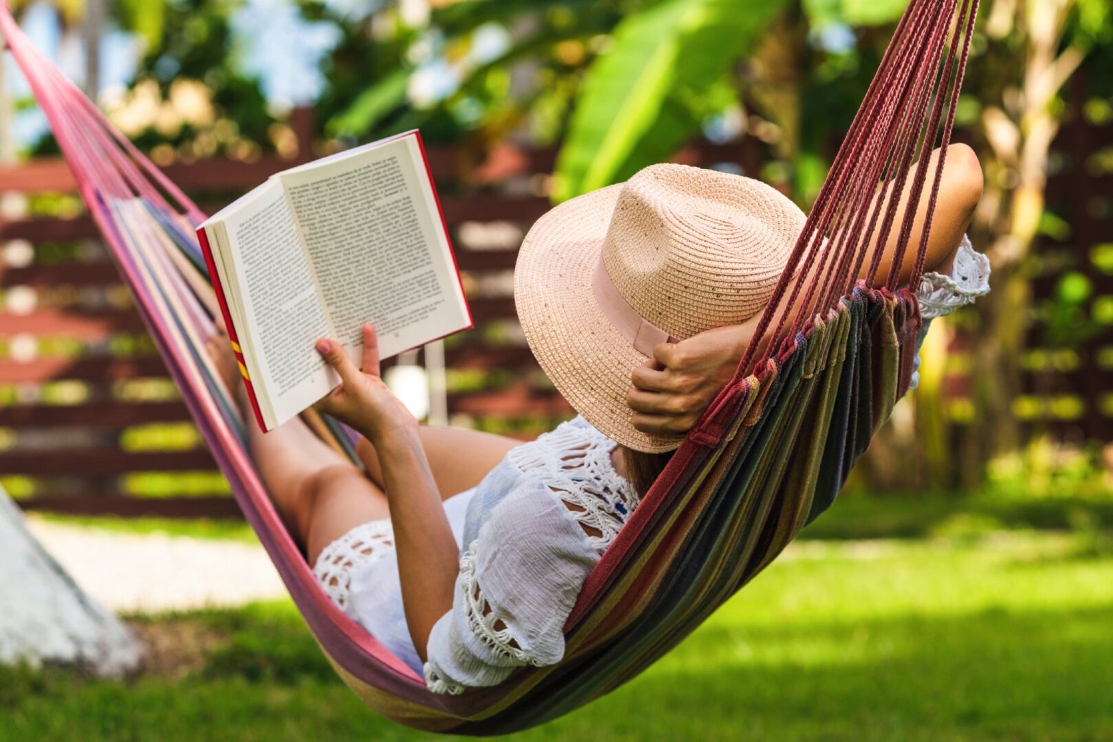Frau liegt in einer Hängematte und liest ein Buch | Credit: iStock.com/StudioMikara