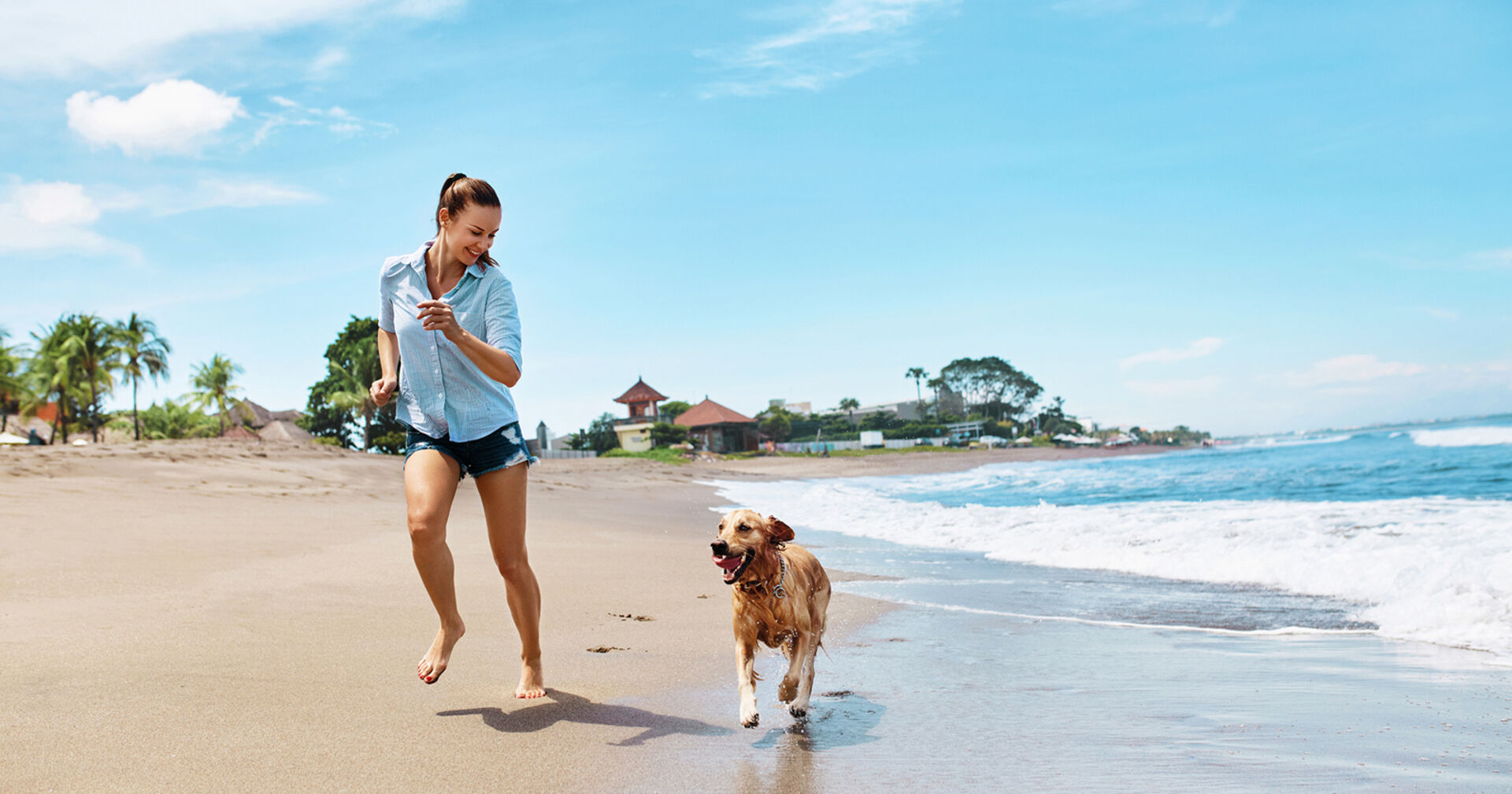 Frau rennt mit Hund am Strand entlang | Credit: iStock.com/puhhha