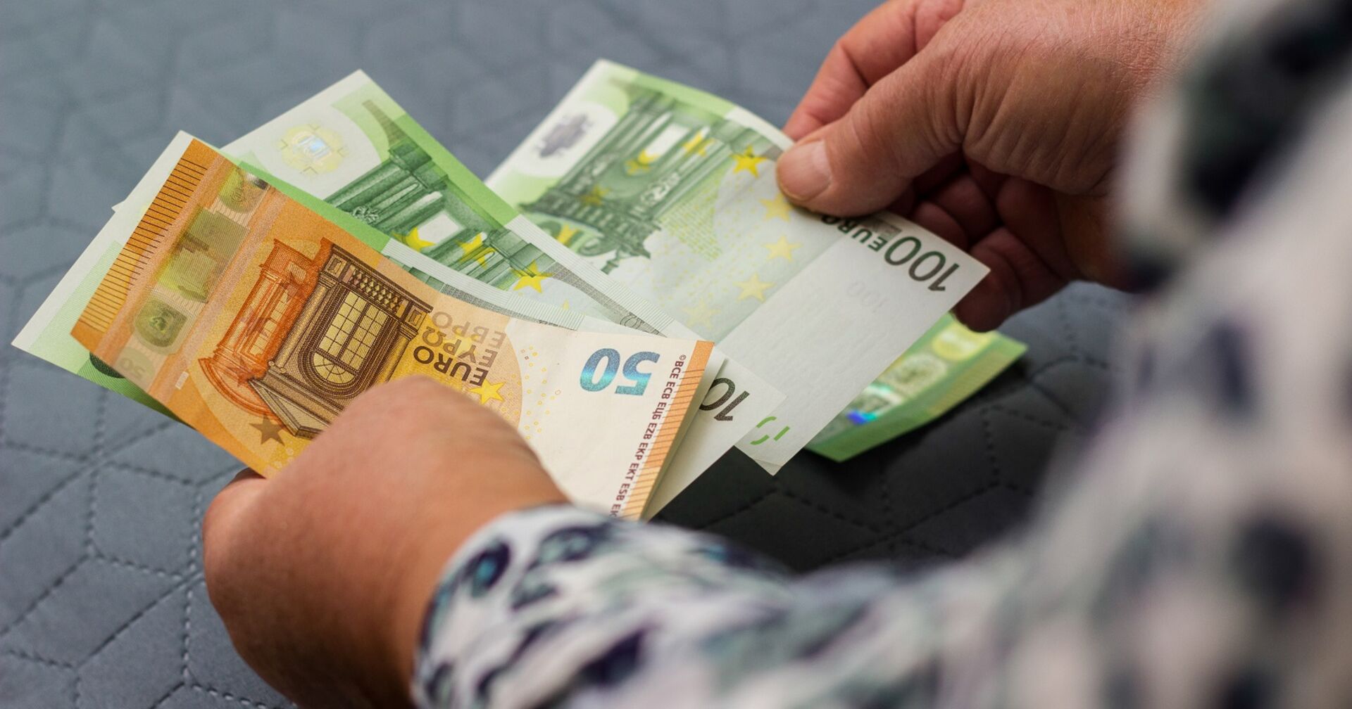 Ein Mann zählt Geldscheine. Er hält einen Fünfzig- und drei 100-Euro-Scheine in der Hand.