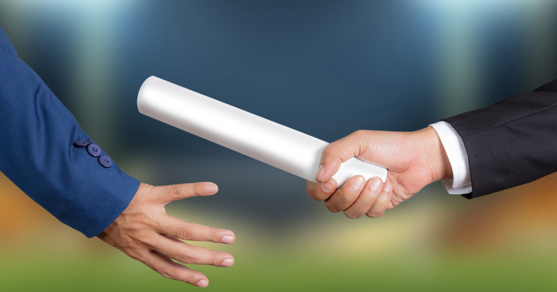 Mann mit schwarzem Anzug gibt Papierrolle an Mann im blauen Anzug weiter | Credit: istock.com/Naypong