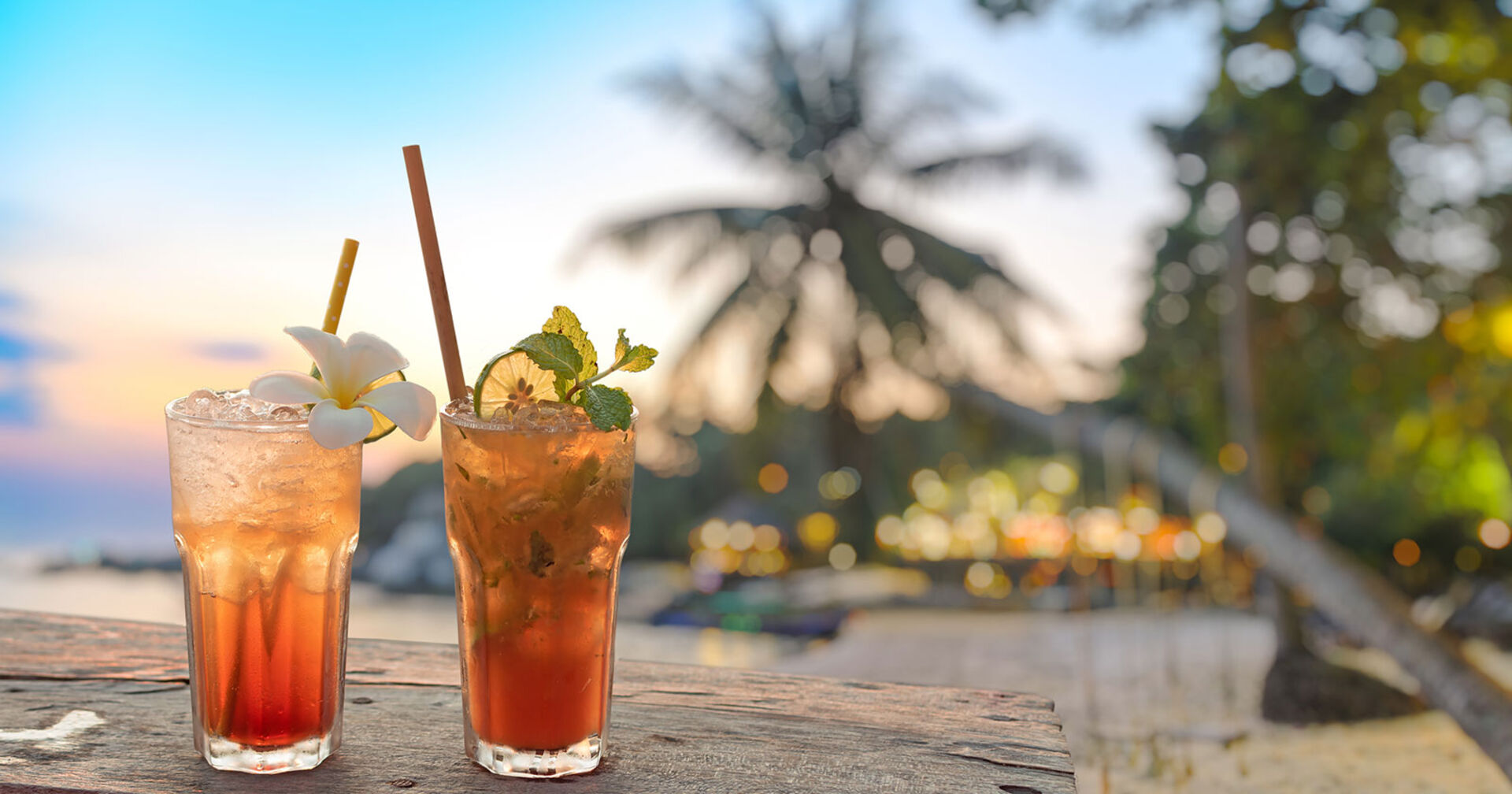 Zwei Gläser mit Limonade und Trinkhalm an einem tropischen Strand bei Sonnenuntergang | Credit: iStock.com/Lichtwolke