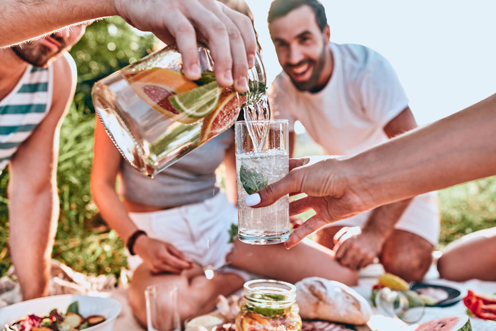 Bei einem gemeinsamen Essen unter freiem Himmel schenkt ein Mann einem anderen ein Glas Wasser ein | Credit: iStock.com/Harbucks