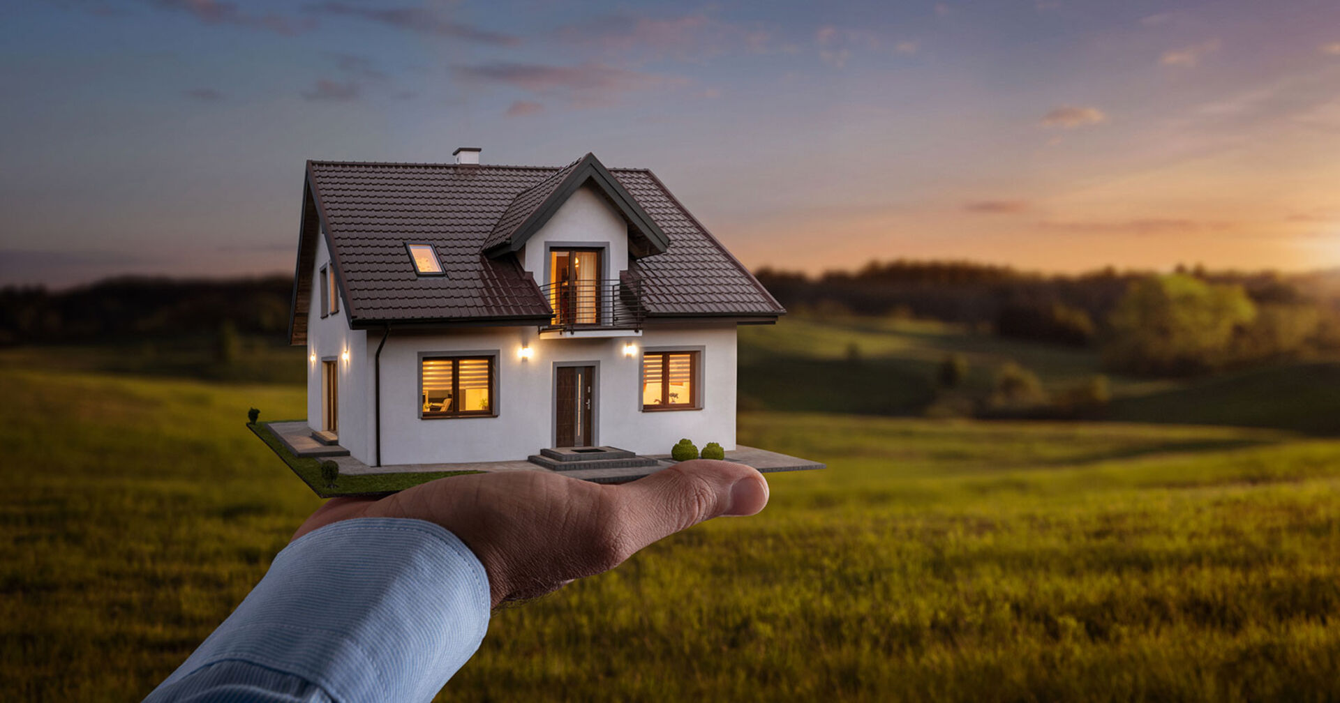 Mann hält beleuchtetes Haus in Miniaturform in seiner Hand | Credit: iStock.com/Nastco