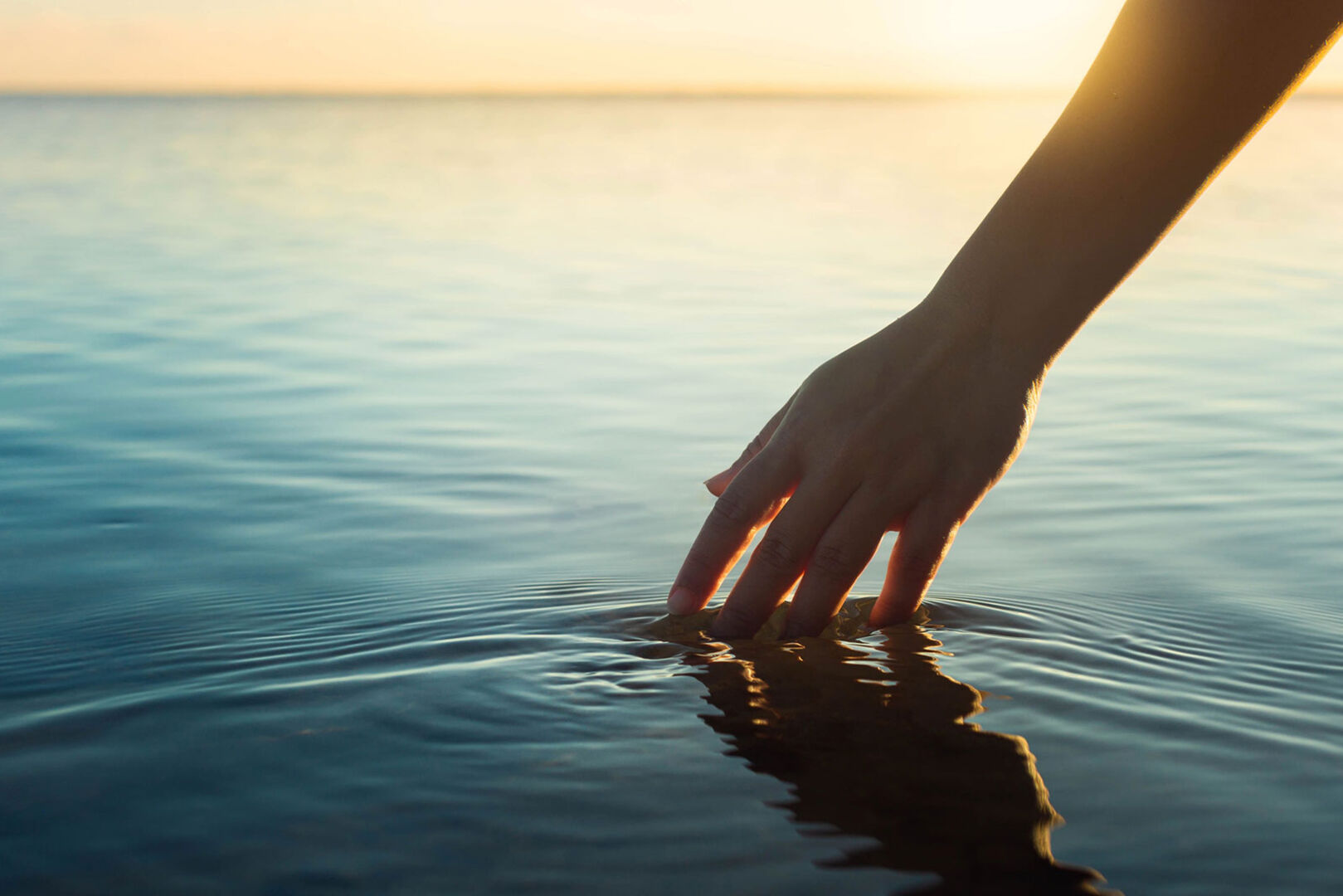 Junge Frau hält ihre Hand in das Wasser eines Sees | Credit: iStock.com/globalmoments