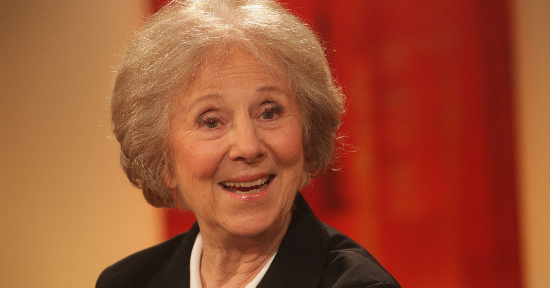 Eine ältere Dame mit weißblonden Haaren lacht in die Kamera.