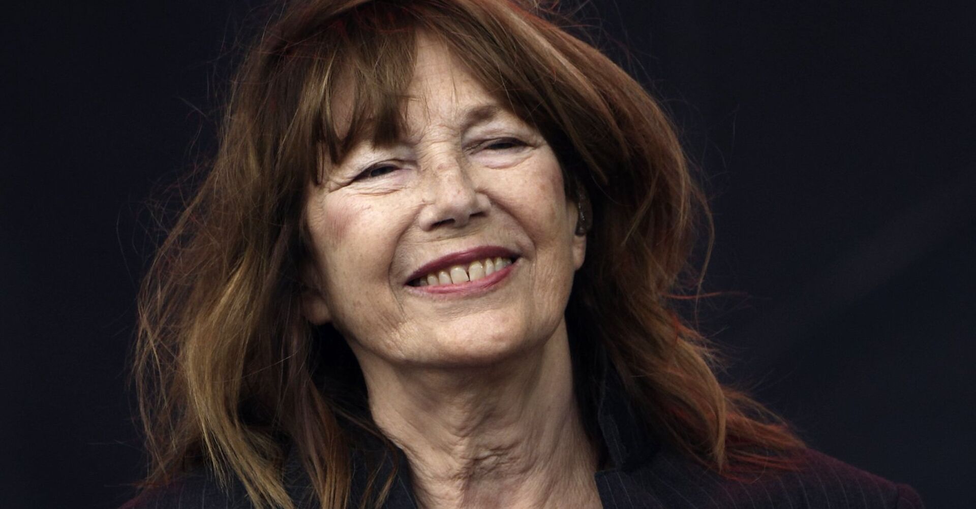 Eine ältere Frau mit braunen Haaren und schwarzem Hintergrund.